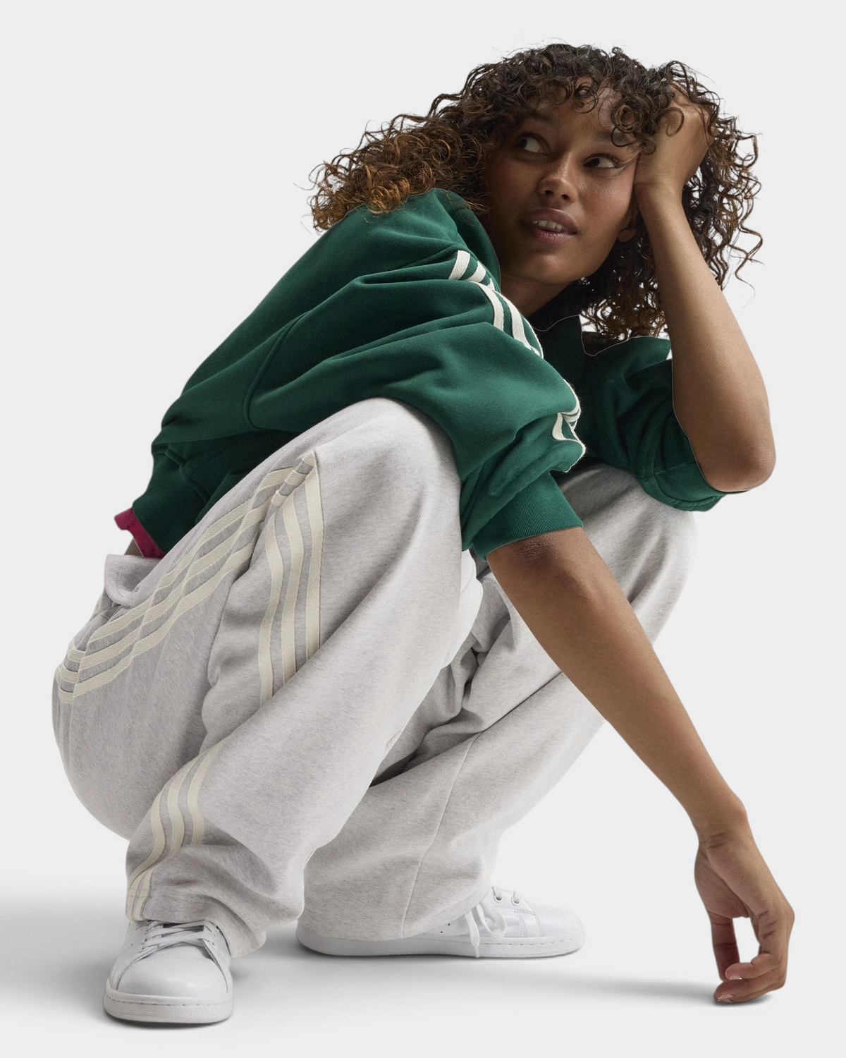 Lockwood Avenue adidas adiSignature 3-Stripes Open Hem Sweatpants in light grey heather, model crouching in a green sweatshirt and white sneakers