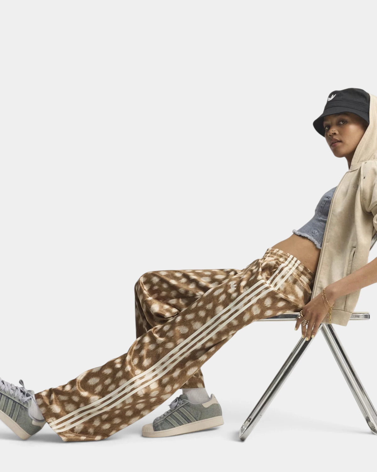 Lockwood Avenue adidas Firebird Animal Print Track Pants worn by a model sitting on a folding chair, legs stretched out, with a cream hoodie and grey sneakers