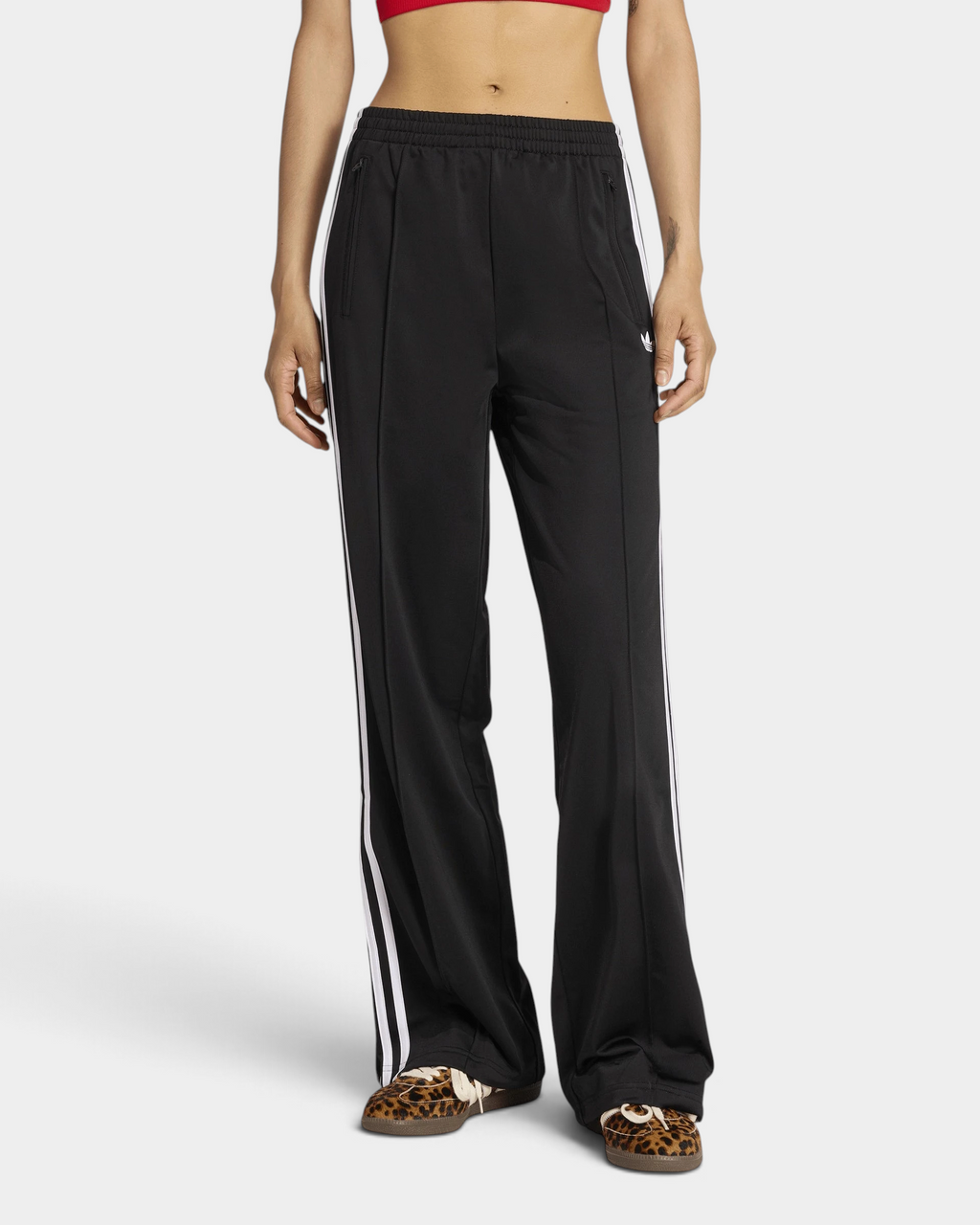 Lockwood Avenue adidas Firebird Loose Track Pants in black worn with leopard-print sneakers, front view from the chest down, straight wide legs with white 3-Stripes