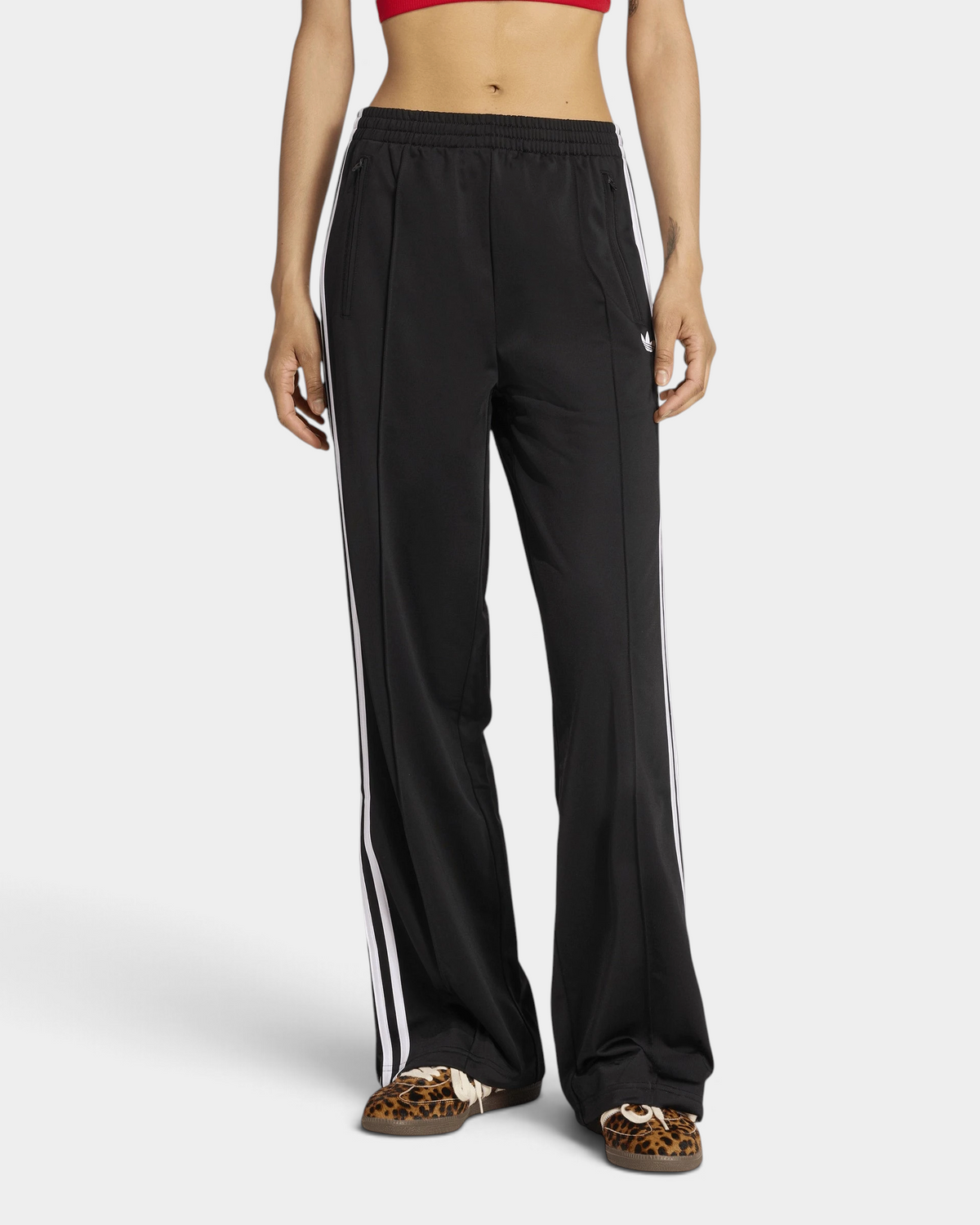 Lockwood Avenue adidas Firebird Loose Track Pants in black worn with leopard-print sneakers, front view from the chest down, straight wide legs with white 3-Stripes