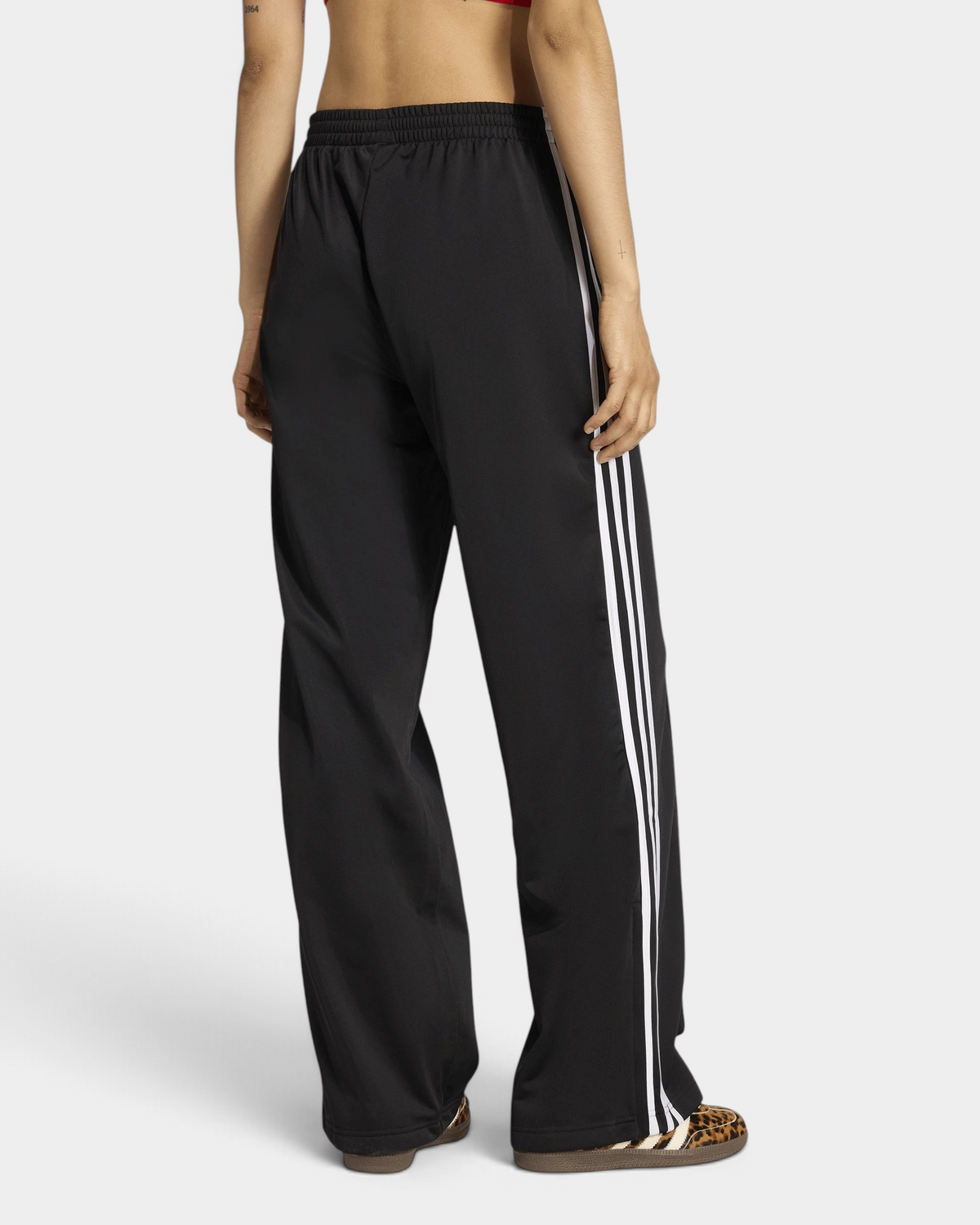 Lockwood Avenue adidas Firebird Loose Track Pants in black seen from behind on a model, white 3-Stripes down the outer leg and leopard-print sneakers