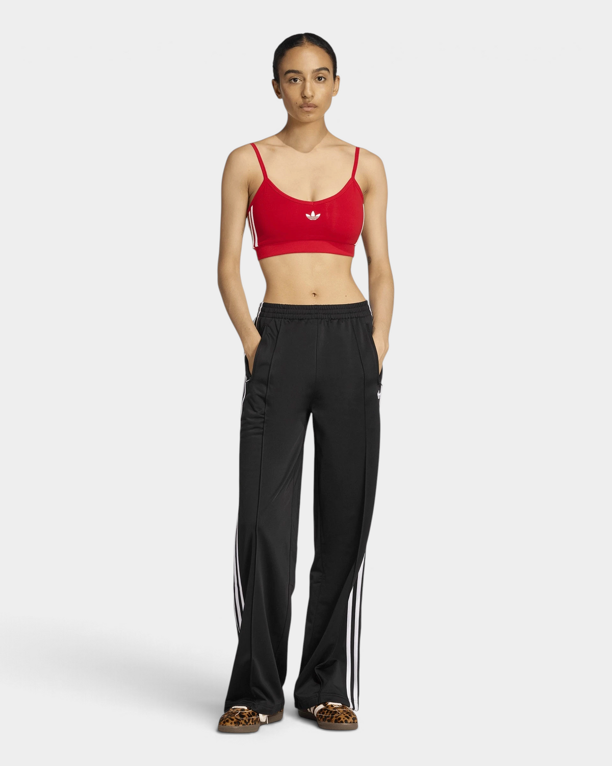 Lockwood Avenue adidas Firebird Loose Track Pants in black, full-length front view with hands in the pockets, worn with a red crop top and leopard-print sneakers