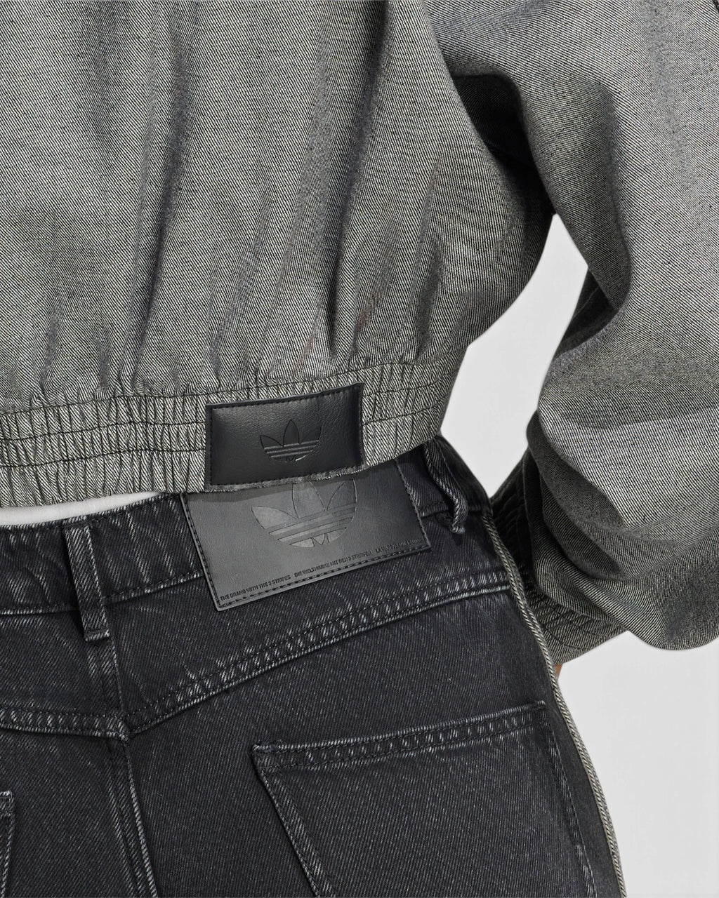Lockwood Avenue adidas SST Denim Track Top close up, the gathered elastic hem of the light grey denim above a pair of black jeans