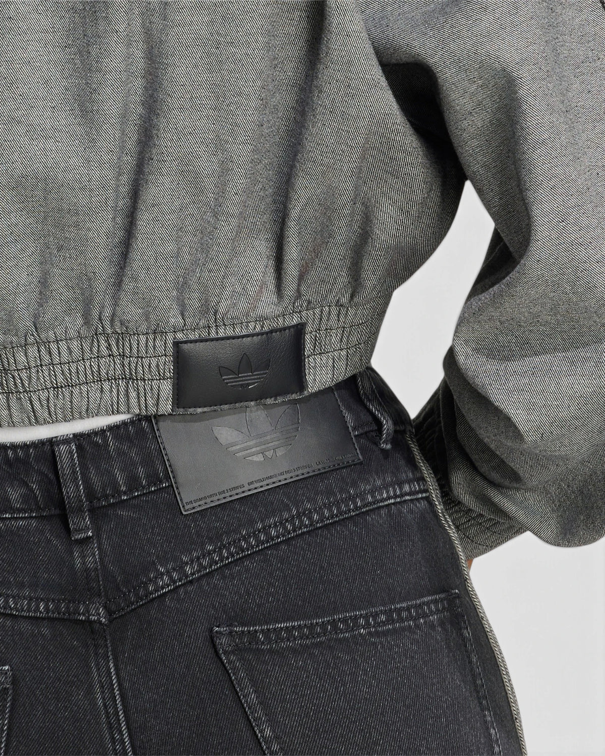 Lockwood Avenue adidas SST Denim Track Top close up, the gathered elastic hem of the light grey denim above a pair of black jeans