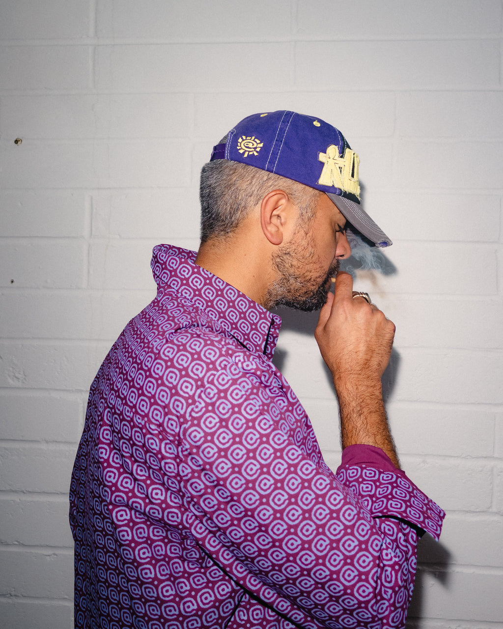 Lockwood Avenue ADWYSD Human Logo 5-Panel Cap in Purple/Black/Yellow worn by a model in a purple patterned shirt, seen from the side