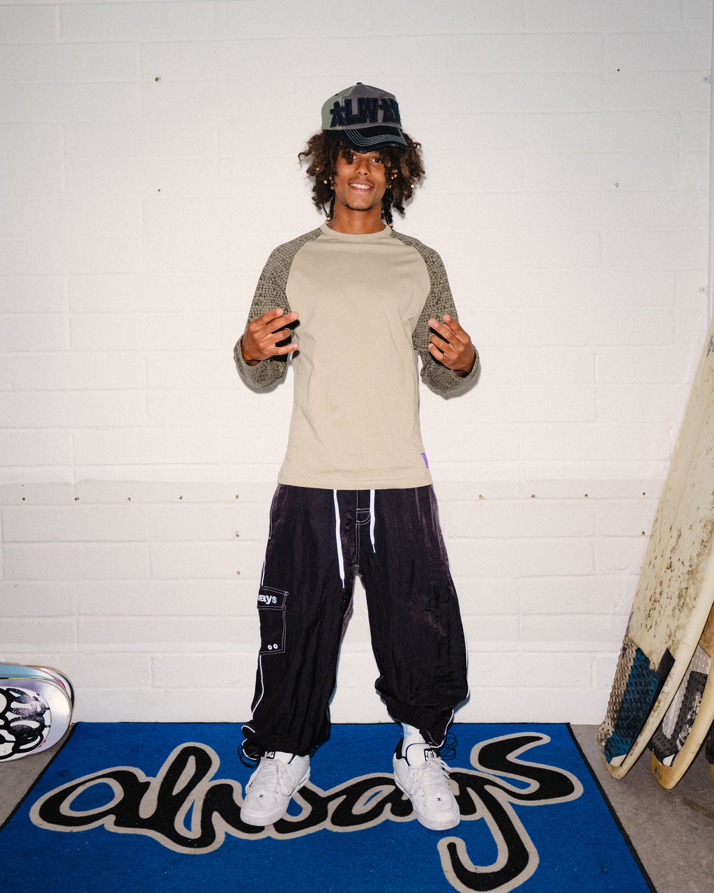 Lockwood Avenue ADWYSD Bubble Print Raglan Long-Sleeve T-Shirt in Two Tone Brown worn by a smiling model with black track pants and a cap