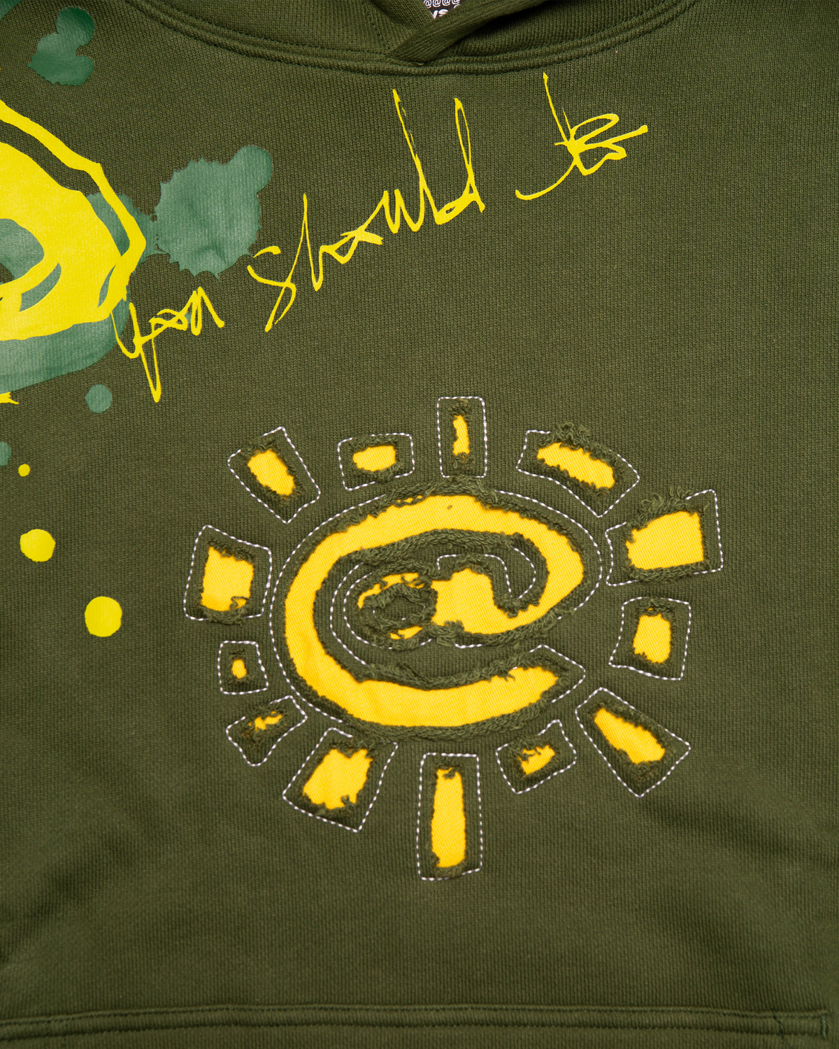 Lockwood Avenue ADWYSD Waza Hoodie in Green, close-up of the yellow @ sun appliqué with white stitching and yellow paint splatter