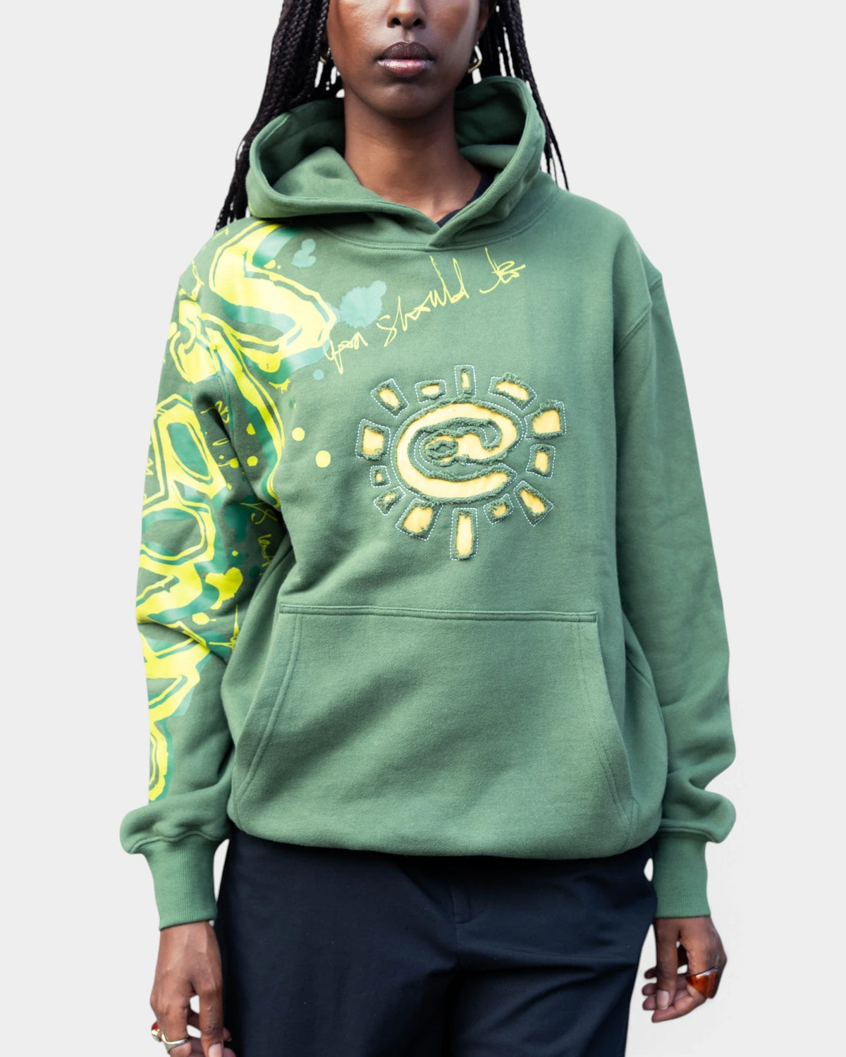 Lockwood Avenue ADWYSD Waza Hoodie in Green, worn by a model, yellow @ sun appliqué on the chest and yellow print down the sleeve