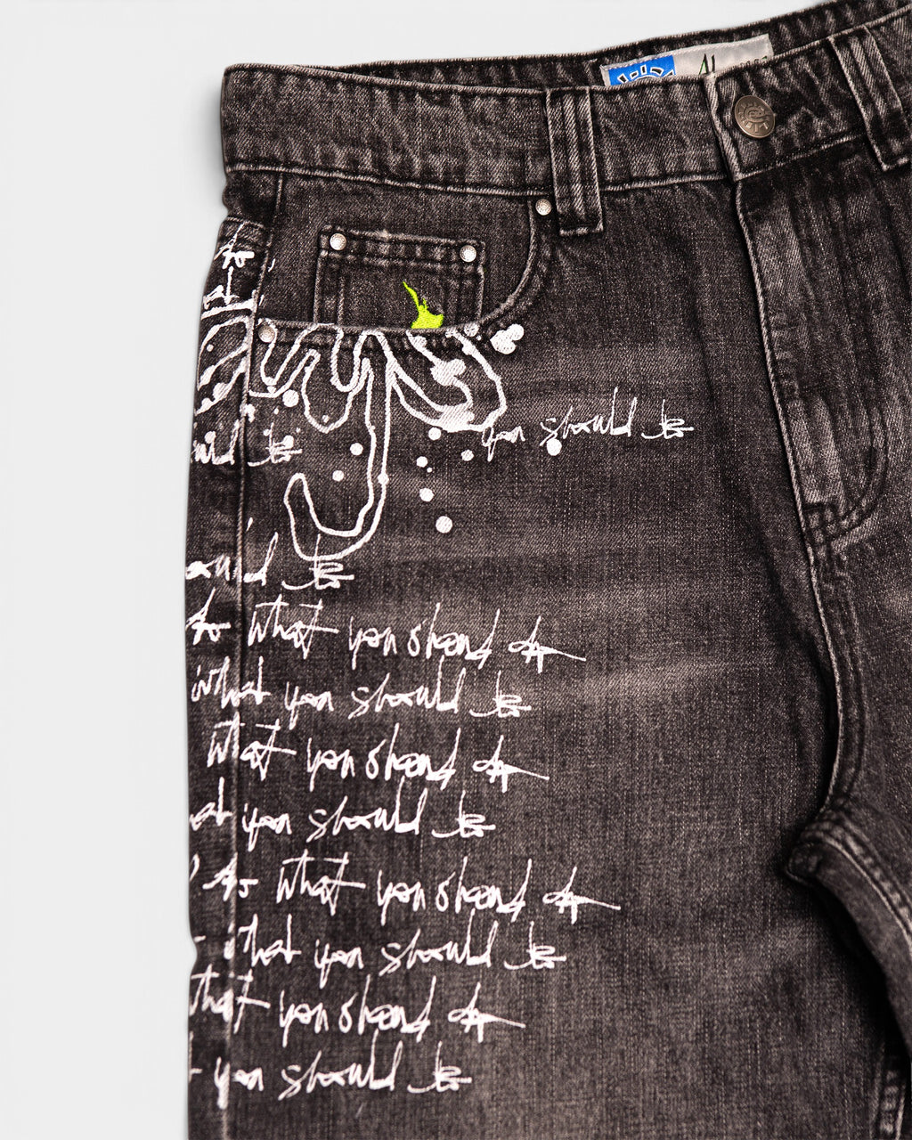 Lockwood Avenue ADWYSD Waza Jeans in Washed Black, close-up of the white script and the small green sun mark on the front pocket