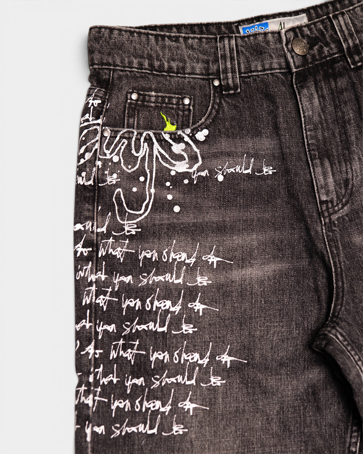 Lockwood Avenue ADWYSD Waza Jeans in Washed Black, close-up of the white script and the small green sun mark on the front pocket