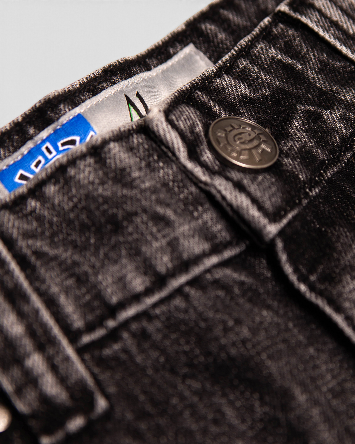 Lockwood Avenue ADWYSD Waza Jeans in Washed Black, close-up of the waistband with a metal @ button and woven labels