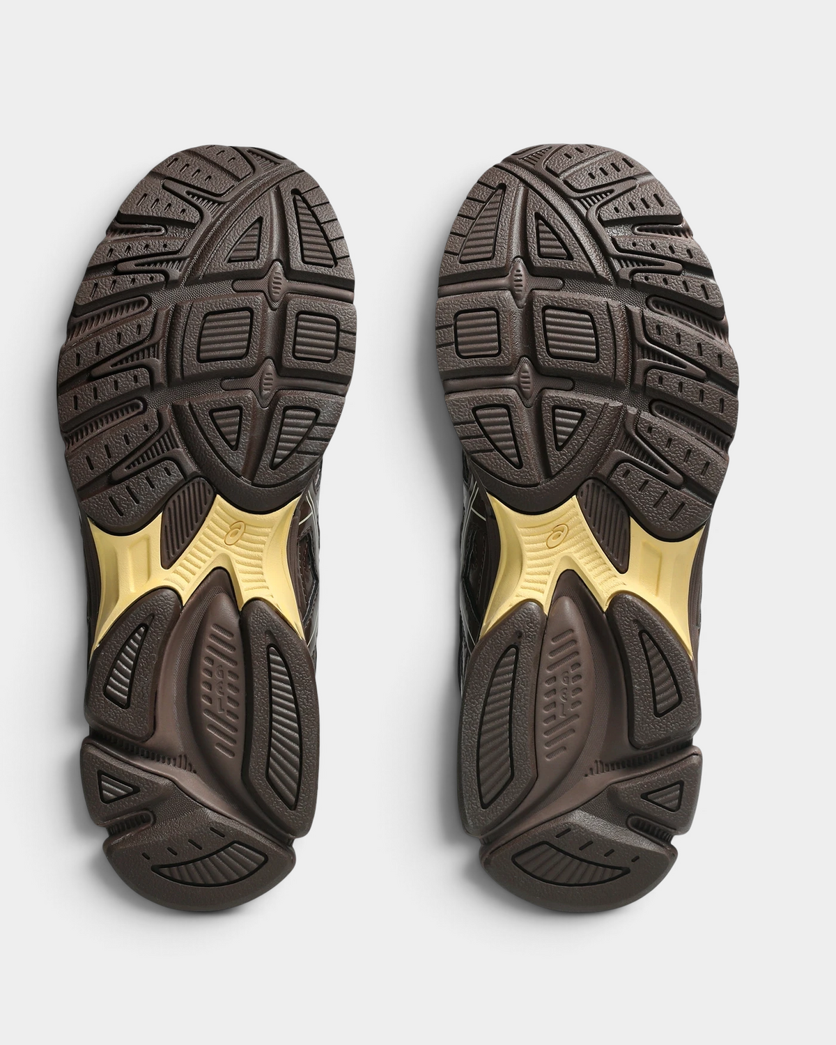 Asics GEL-Stratus MC Shoes in Brown Storm, outsoles of the pair: dark brown rubber with raised tread blocks and yellow-gold sections under the heel and forefoot