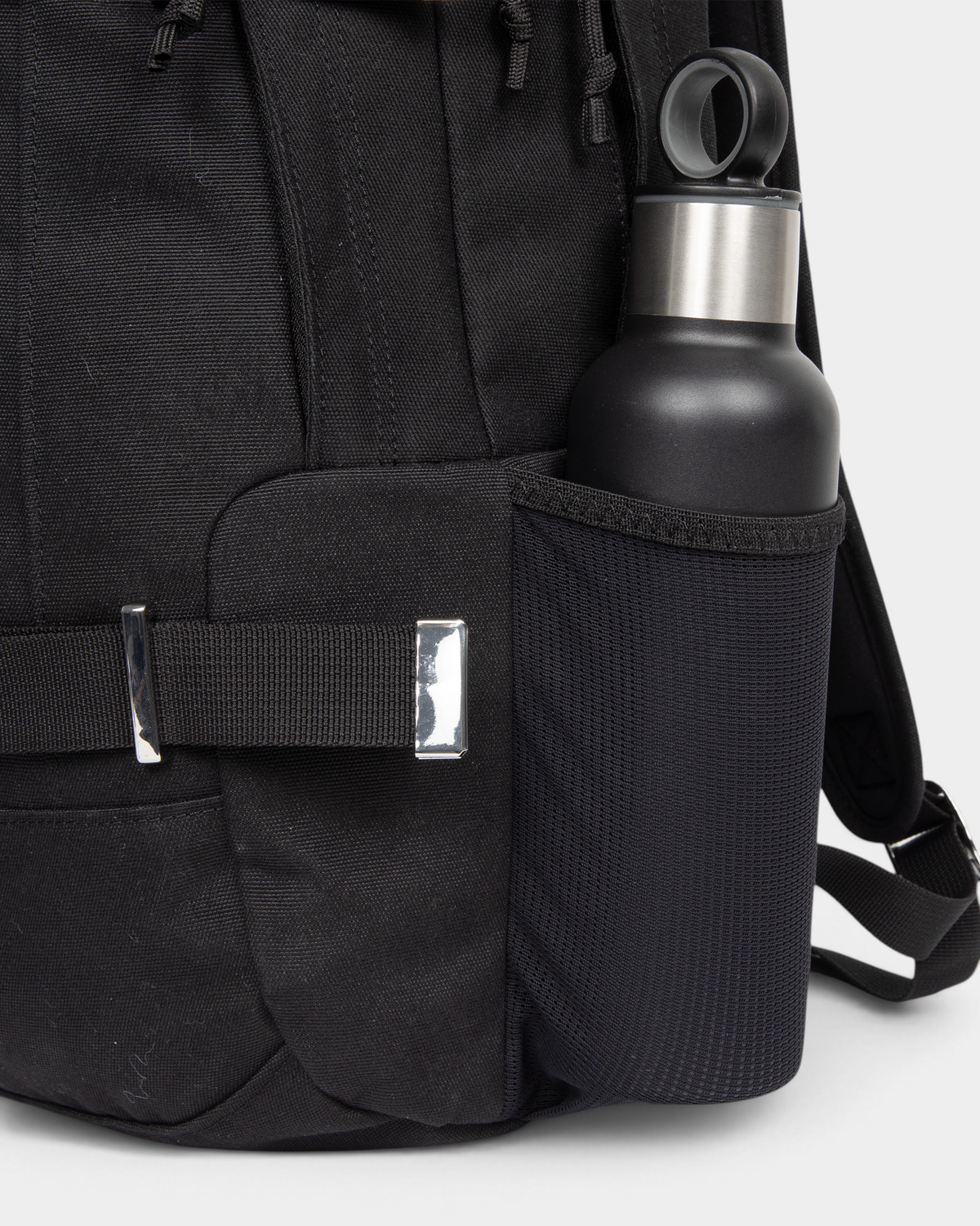 Side view of the Eastpak x Dime Getter Backpack in Dime Black with a water bottle in the elasticated mesh side pocket, next to the polished strap keeper