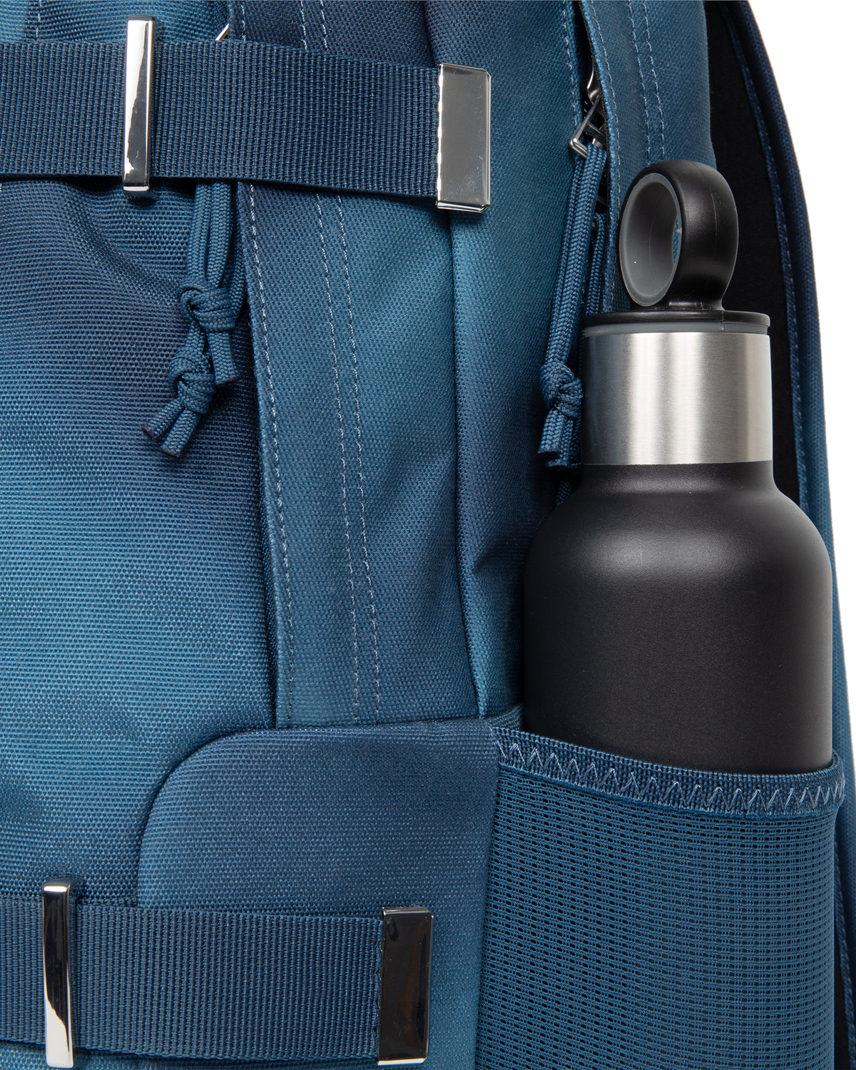 Side view of the Eastpak x Dime Getter Backpack in Dime Navy with a water bottle in the elasticated mesh side pocket, next to the polished strap keeper