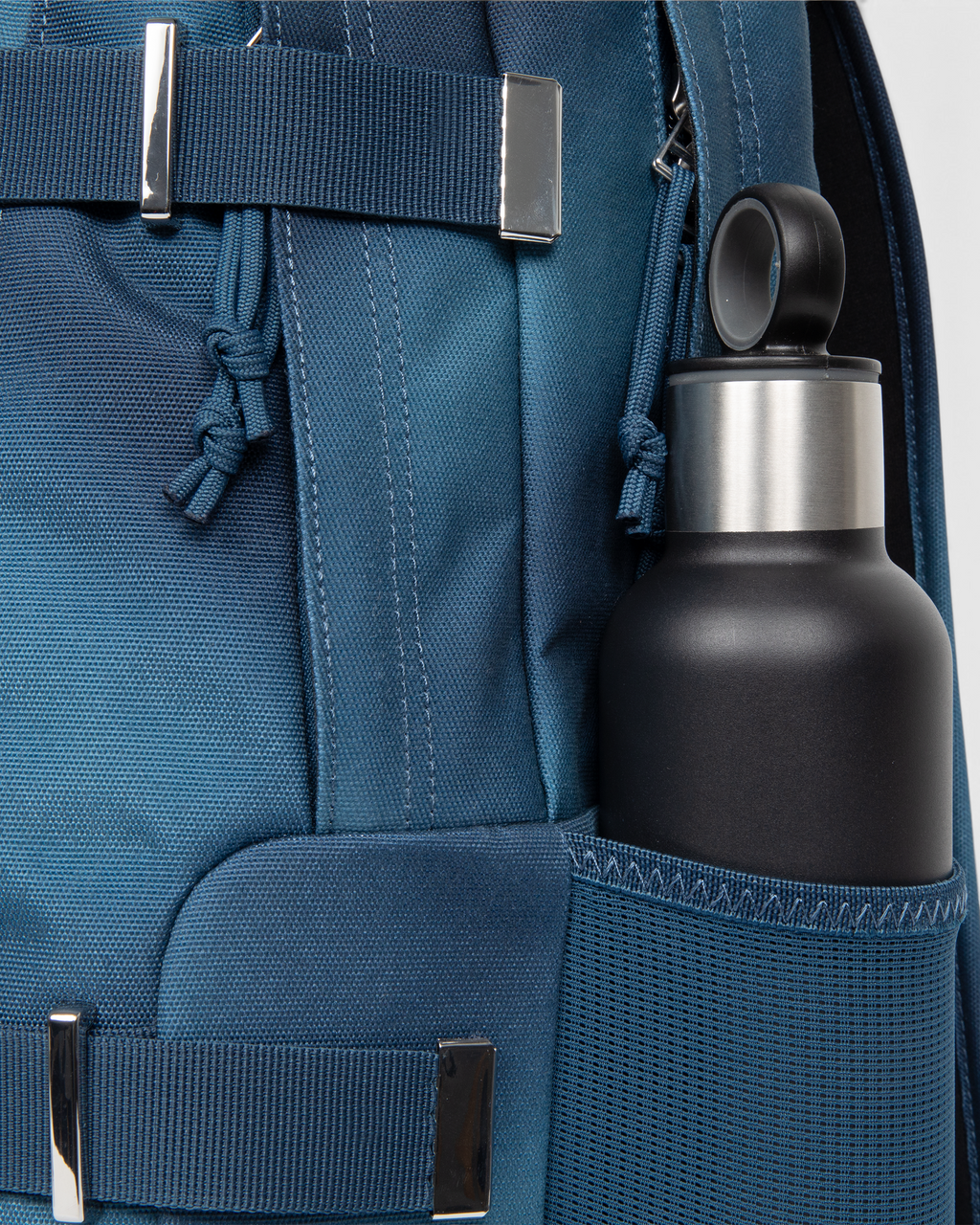 Side view of the Eastpak x Dime Getter Backpack in Dime Navy with a water bottle in the elasticated mesh side pocket, next to the polished strap keeper