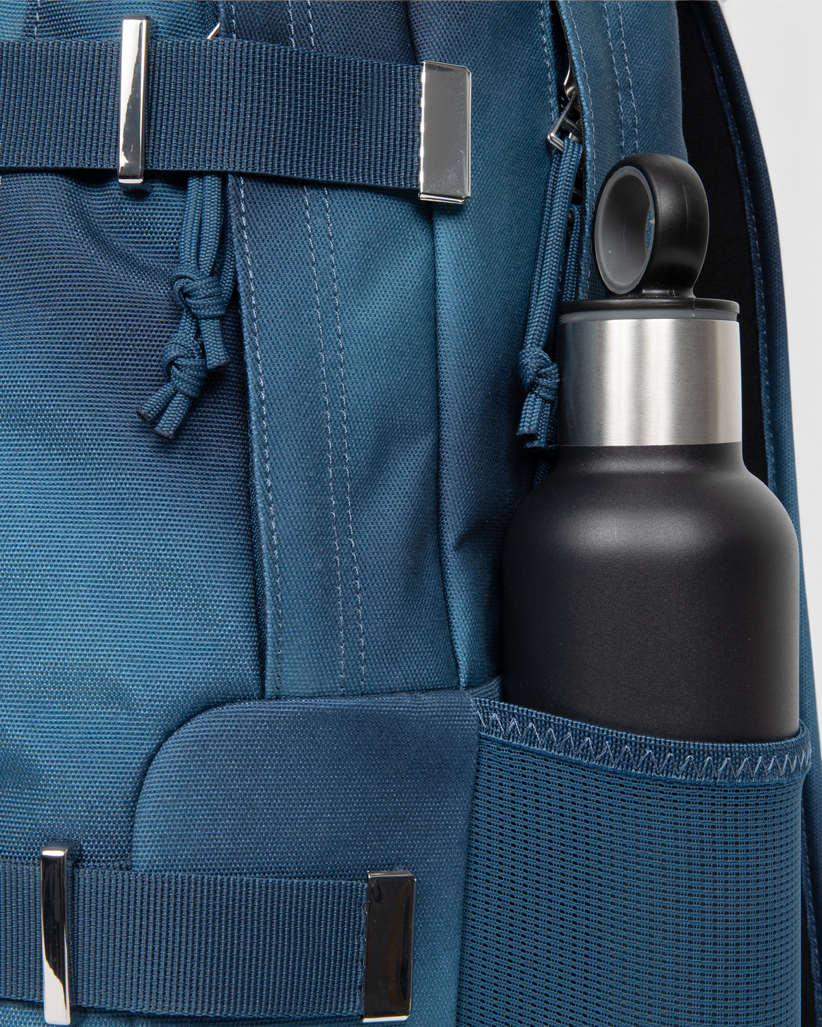 Side view of the Eastpak x Dime Getter Backpack in Dime Navy with a water bottle in the elasticated mesh side pocket, next to the polished strap keeper