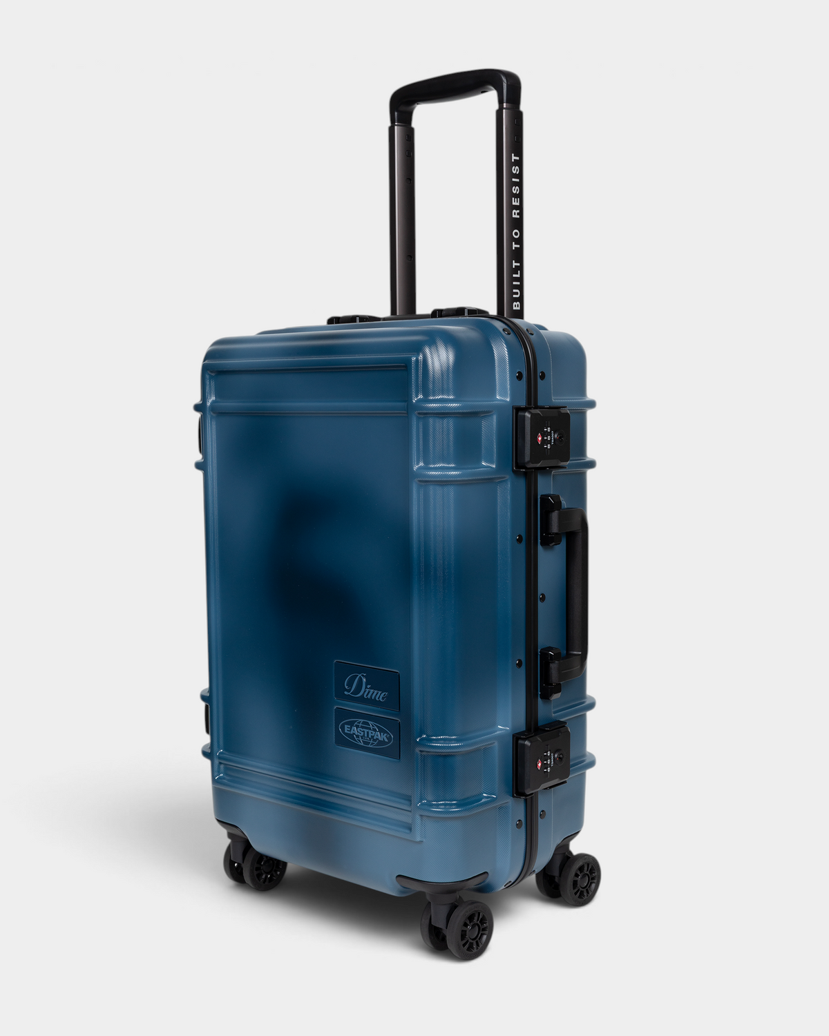 Eastpak x Dime Resist'R Case S in Dime Navy seen from the front three-quarter angle, showing the black aluminium frame edge, two TSA combination locks and the side grab handle, with BUILT TO RESIST printed up the handle stem
