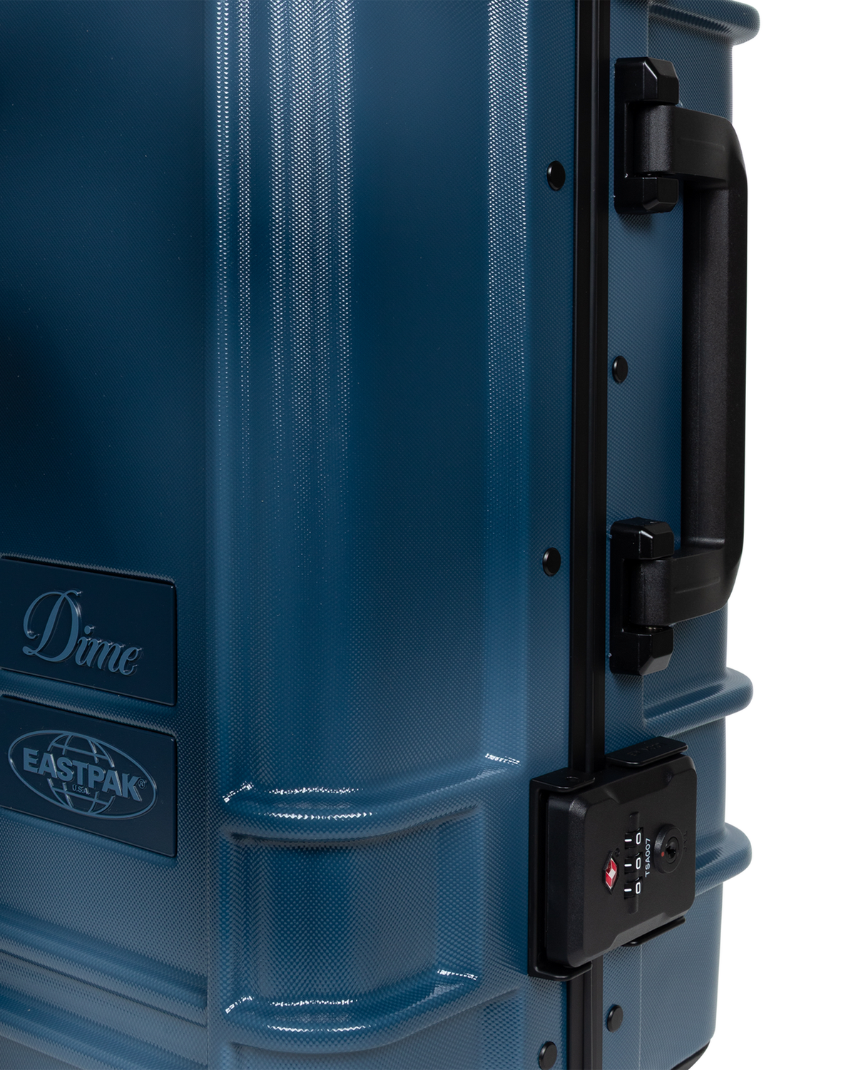 Close up of the side of the Eastpak x Dime Resist'R Case S in Dime Navy, showing the moulded side grab handle, a TSA combination lock and the Dime and Eastpak badges on the brushed navy shell