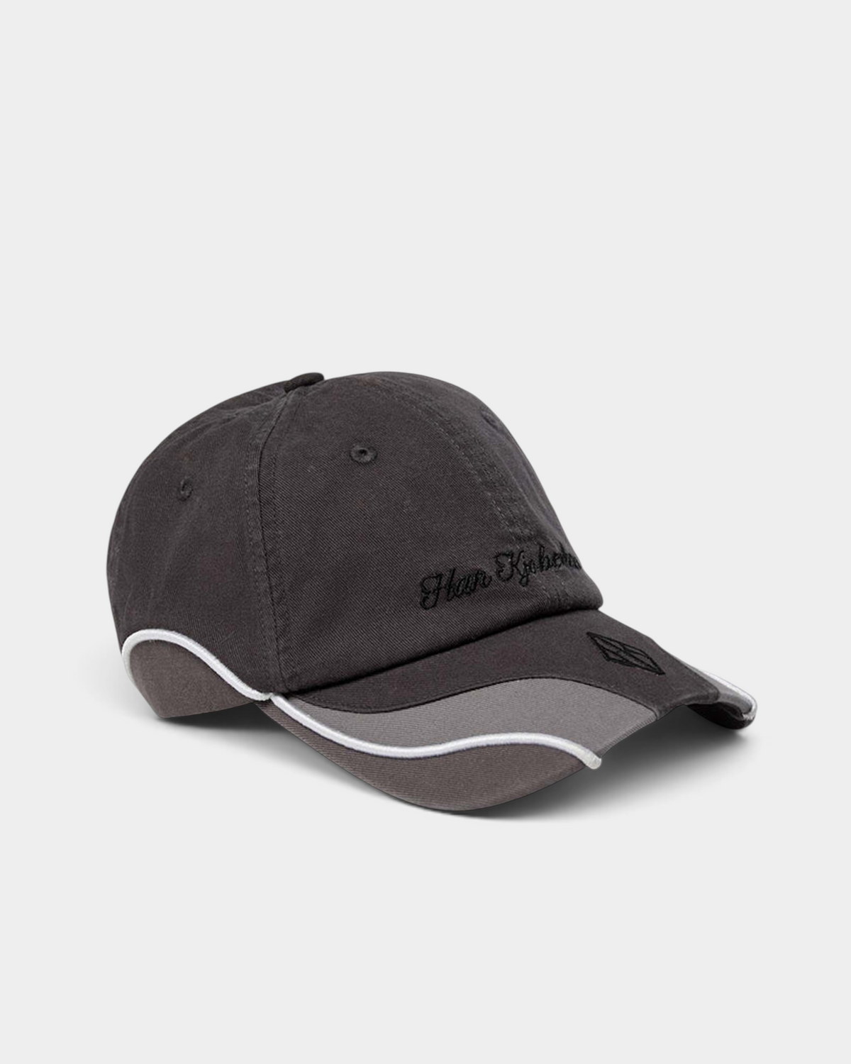 Han Kjøbenhavn Retro Cap in Stone Grey seen from the front at an angle, showing the script logo embroidery on washed grey twill and the contrast panel and piping along the brim