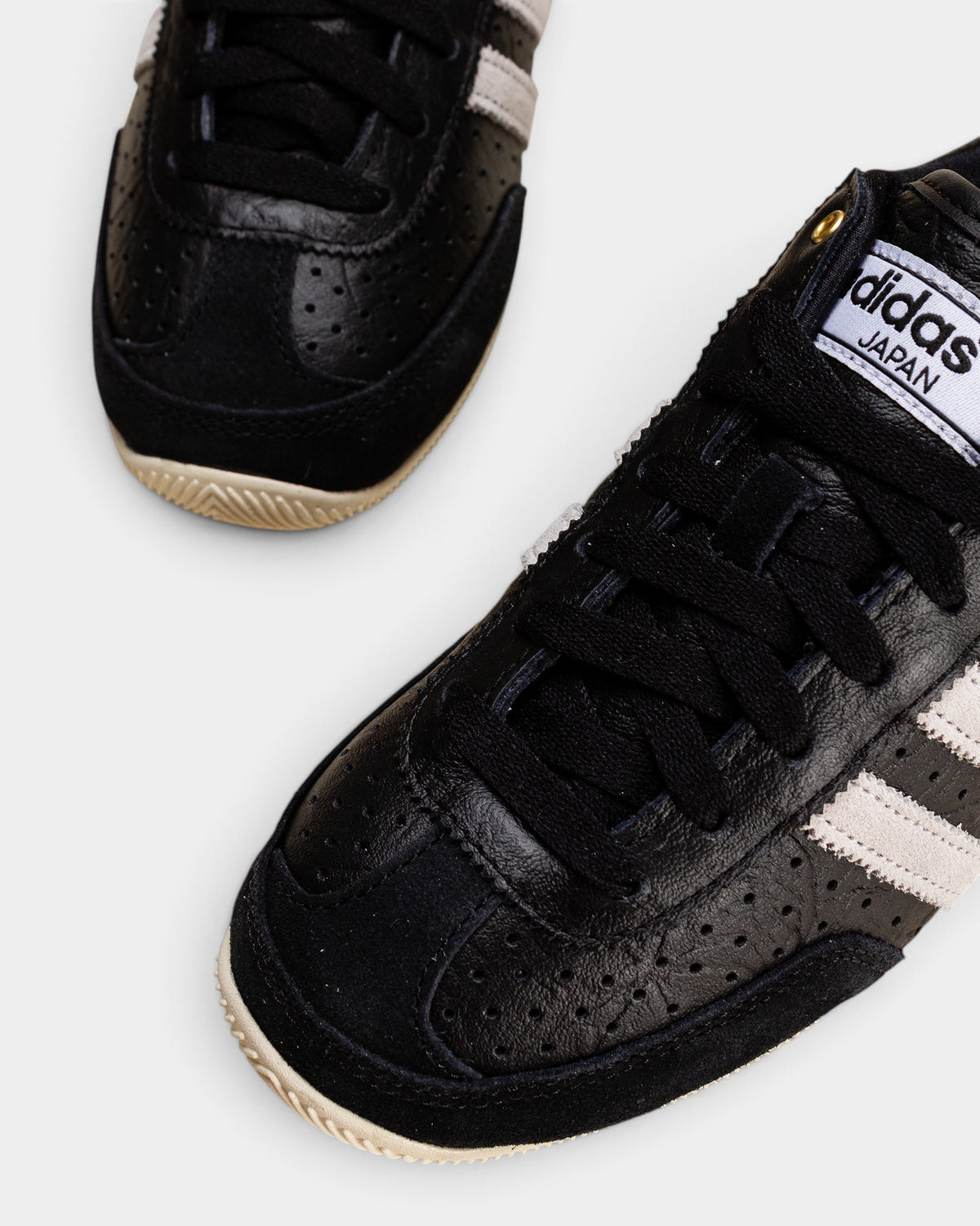 Lockwood Avenue adidas Japan women's black perforated leather trainers with white stripes and gold logo detailing.