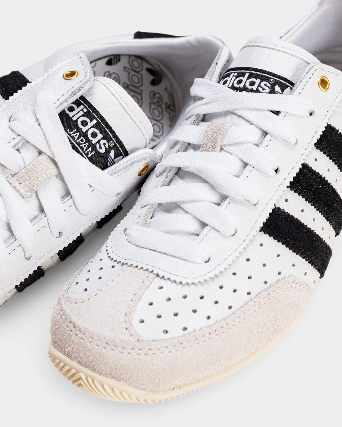 Lockwood Avenue adidas Japan W women's white perforated leather trainer with black stripes and gold eyelet details.