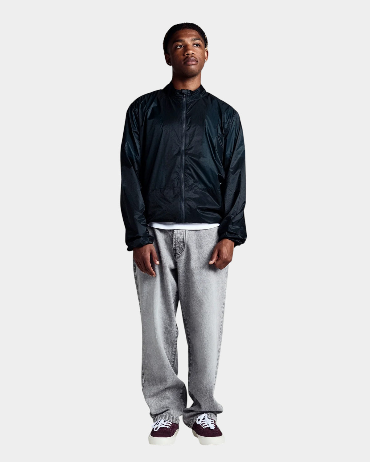 Lockwood Avenue model wearing a black nylon Pop Trading Company team jacket with zip pockets and elasticated cuffs.