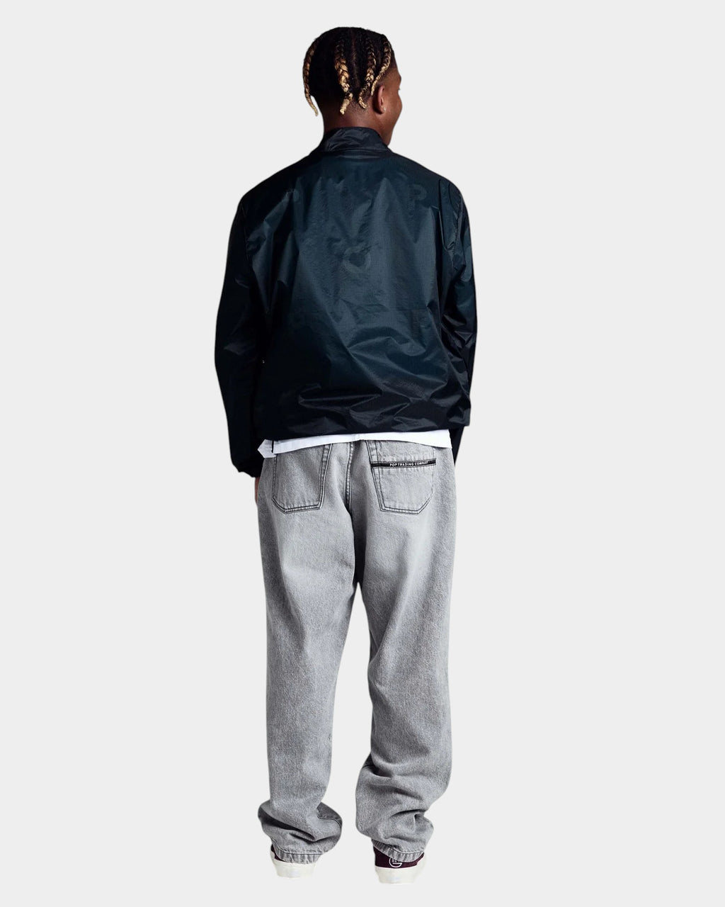 Model wearing a black Lockwood Avenue Pop Trading Company nylon team jacket with elasticated cuffs and hem, back view.