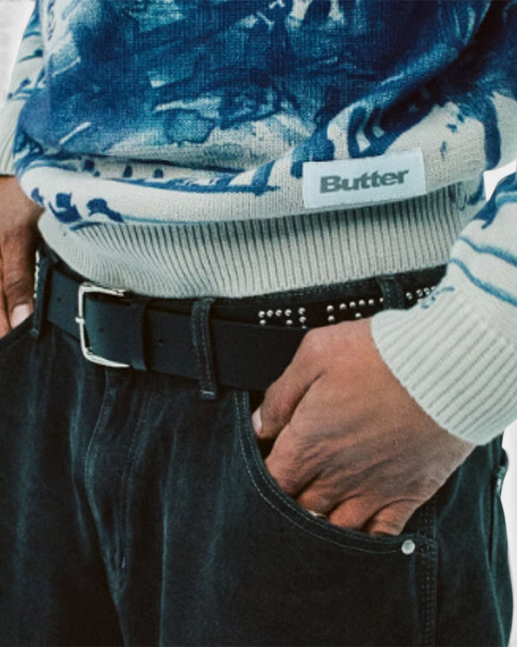 Lockwood Avenue Butter Goods black PU leather belt with metal stud edges and a silver buckle worn with dark trousers.