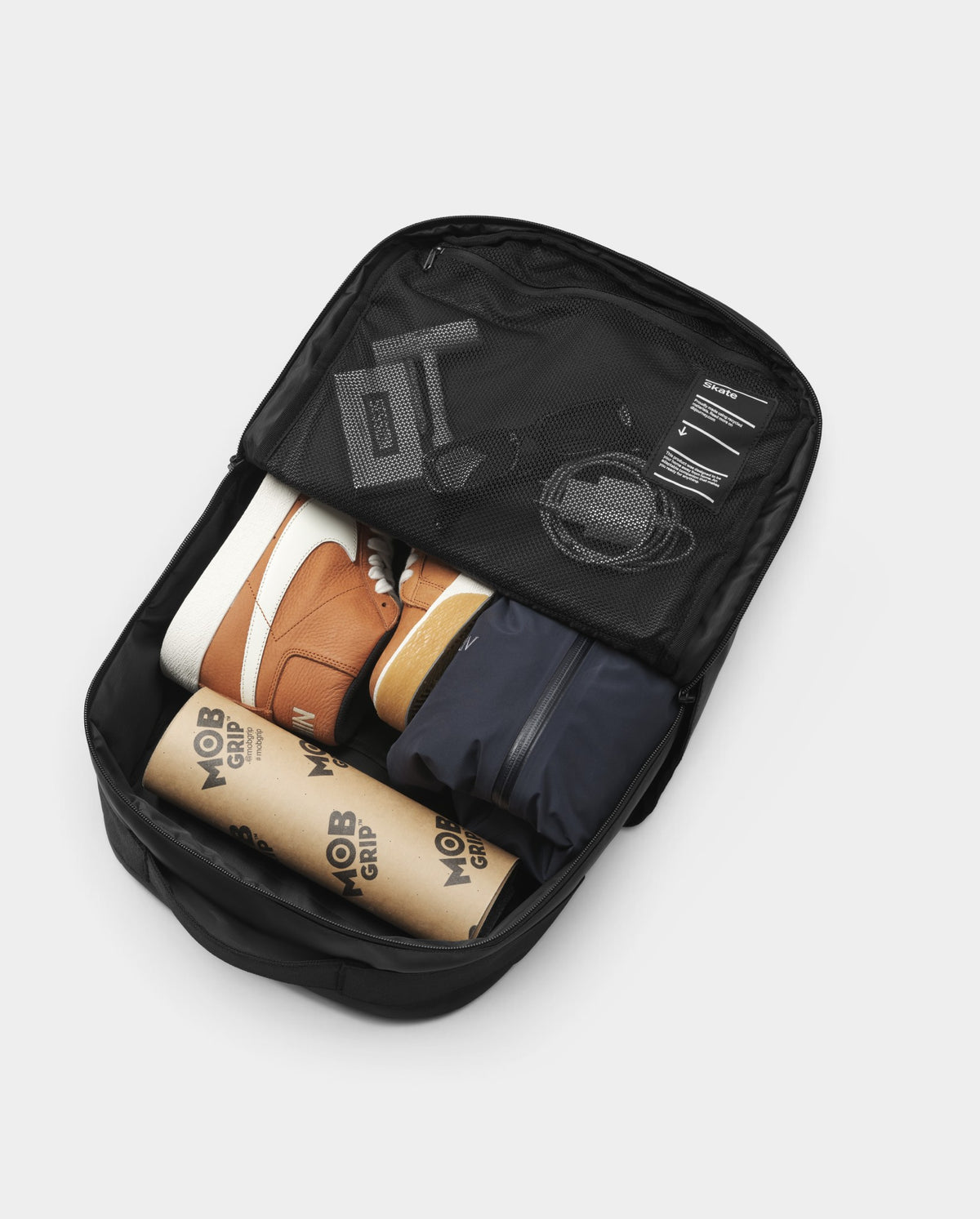 Lockwood Avenue DB Journey 20L daypack open with interior mesh pocket, skate shoes, and grip tape roll inside