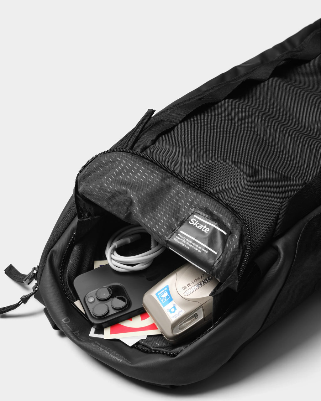 Lockwood Avenue DB Journey Skate 32L carrier in black with open top pocket containing a smartphone and camera