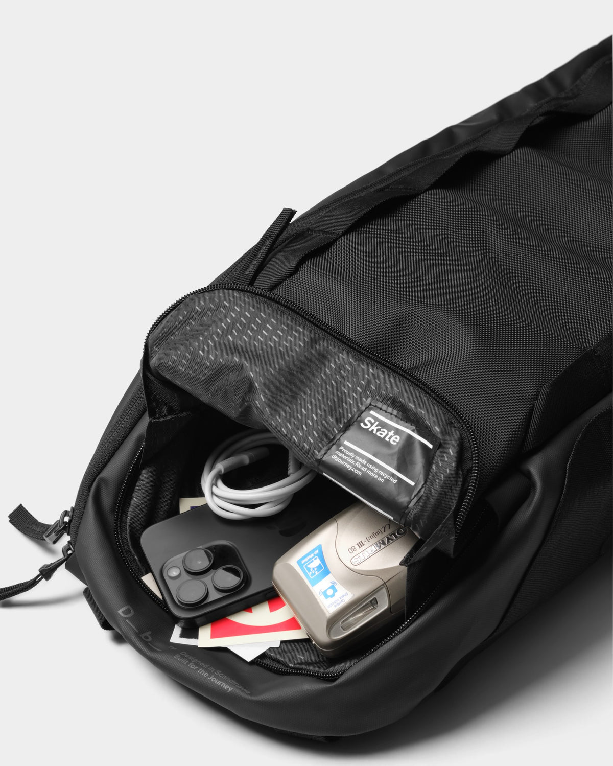 Lockwood Avenue DB Journey Skate 32L carrier in black with open top pocket containing a smartphone and camera