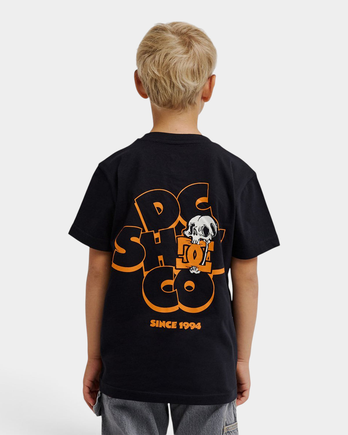 A young boy wearing a black Lockwood Avenue DC Cartoon Jaws youth t-shirt with a large orange and white skull graphic.