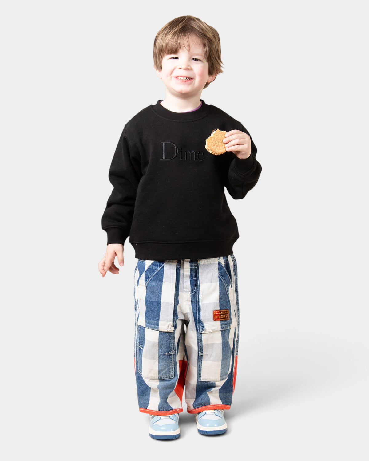 Lockwood Avenue kids black crewneck sweatshirt with embroidered Dime logo, worn by a smiling child.