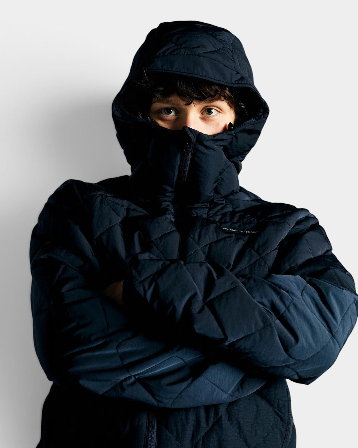 Lockwood Avenue Pop Trading Company navy blue quilted nylon hooded jacket worn by a model with arms crossed