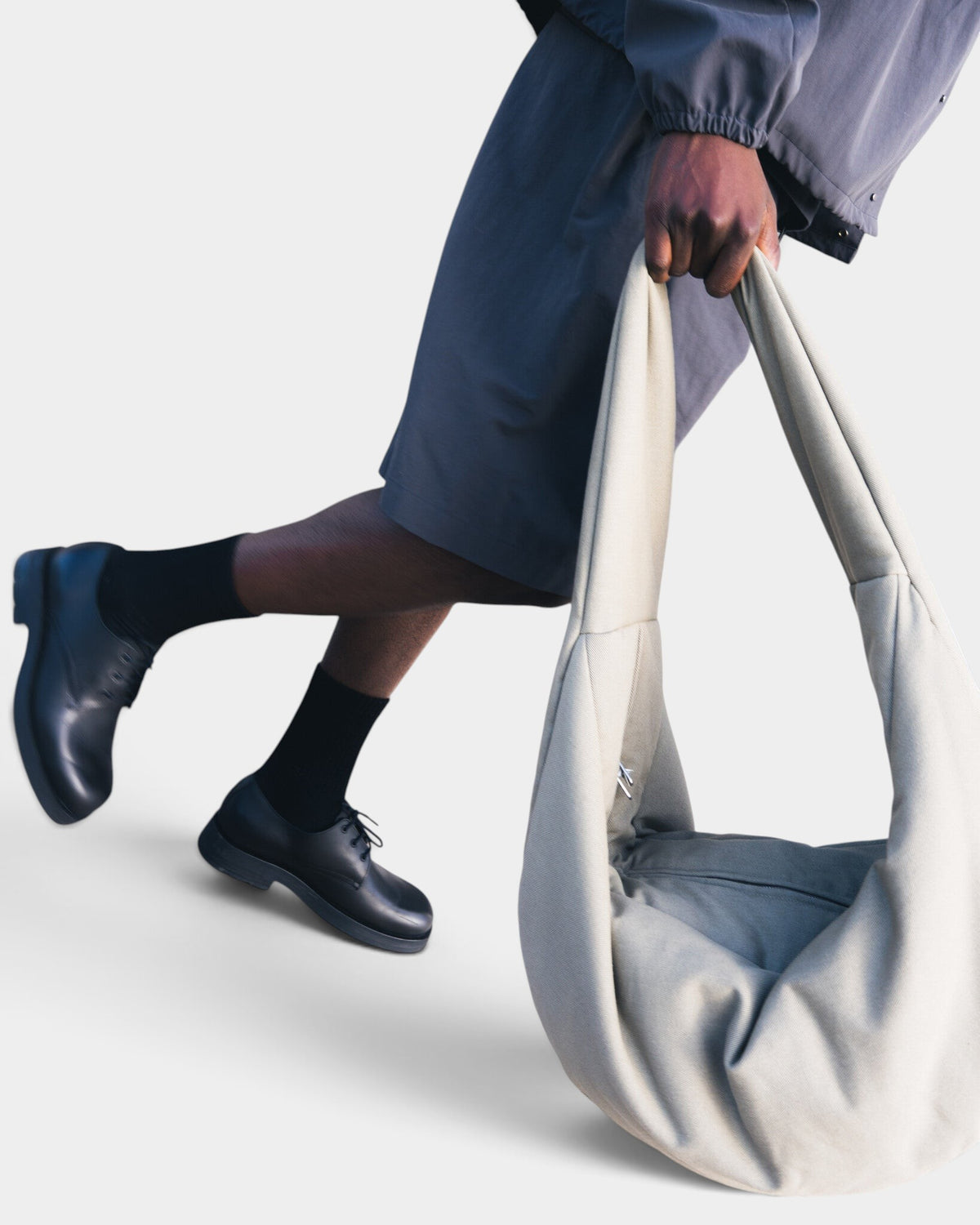 Lockwood Avenue Seventh XL Moon Sac in mushroom, a padded crescent-shaped shoulder bag held by a model.