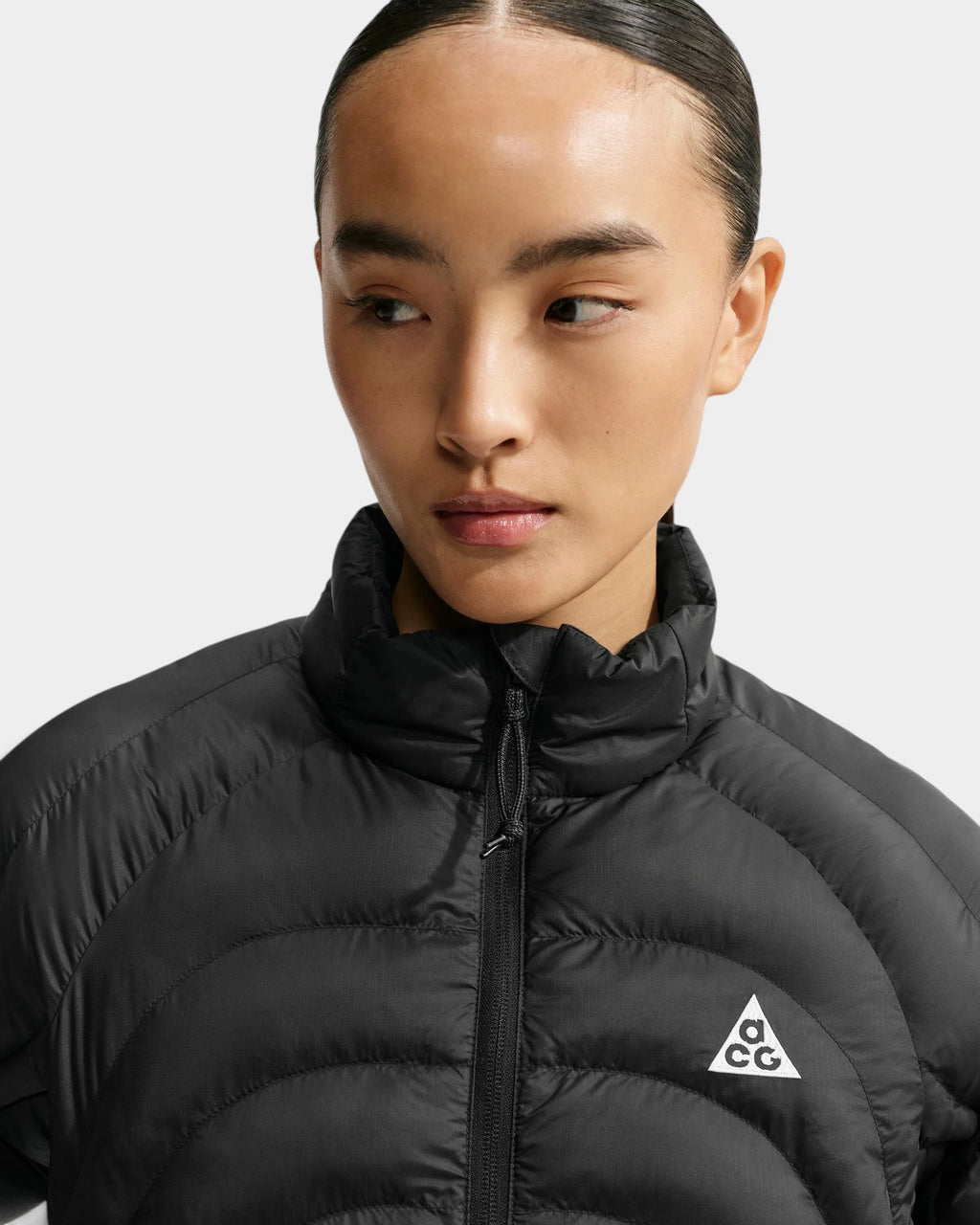 Close up of the Nike ACG Lava Flow Women's Jacket in black and summit white, showing the stand collar, zip and white ACG triangle logo on the chest