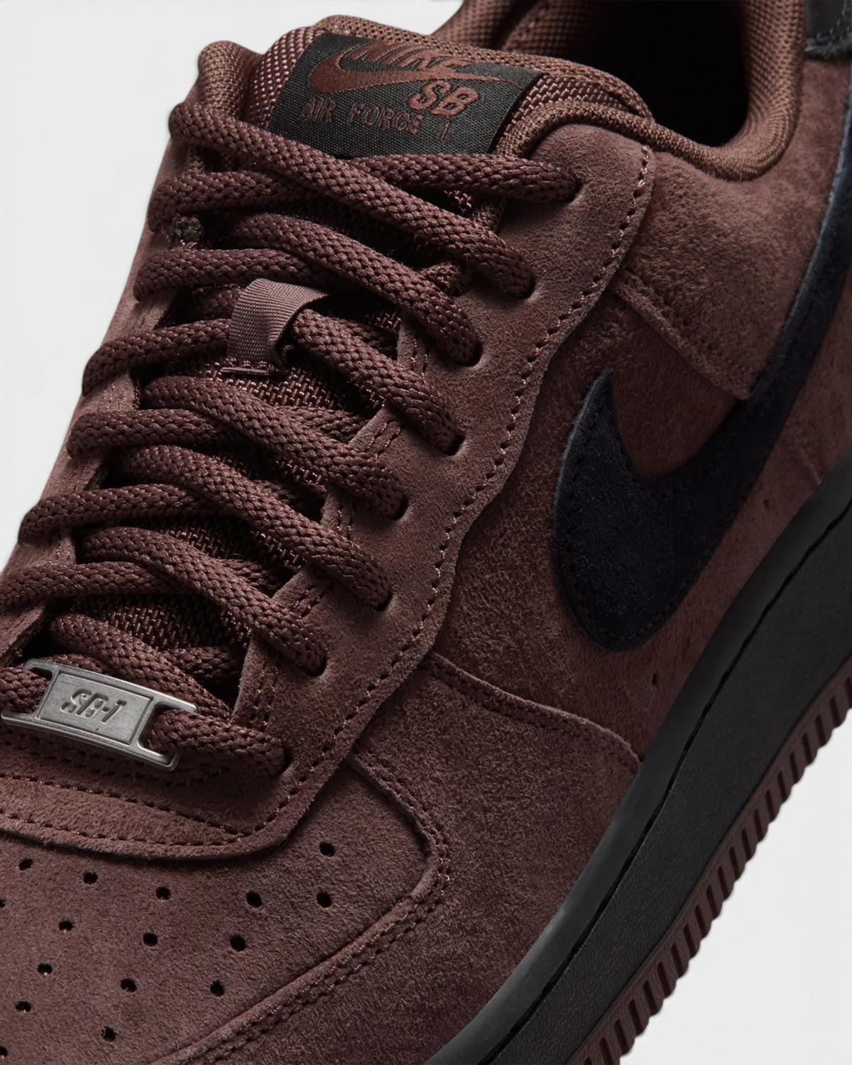 Lockwood Avenue Nike SB Air Force 1 close-up on Light Chocolate suede, the black Swoosh, brown laces and the metal AF1 lace dubrae