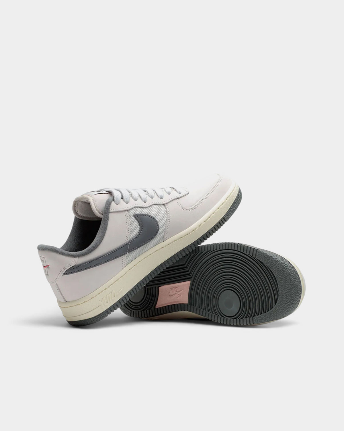 Lockwood Avenue Nike SB Air Force 1 Yuto angled pair, one shoe tipped to show the dark grey outsole and the coral heel panel