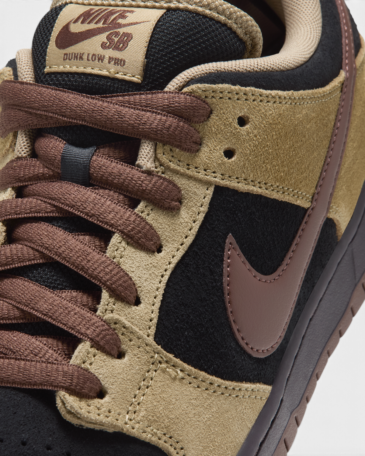 Nike SB Dunk Low Pro Shoes in Filbert/Light Chocolate/Black/Burgundy Ash, close-up of the brown laces, the Dunk Low Pro SB tongue label, the brown Swoosh and the stitched tan suede