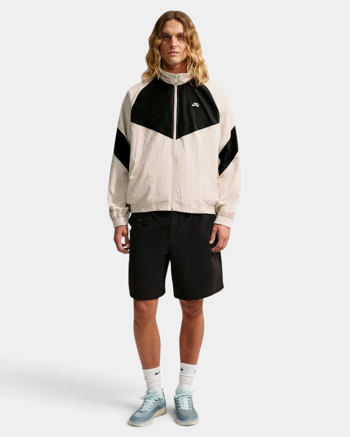 Model wearing the Nike SB Pavan Jacket in light orewood brown and black, zipped up with black shorts, full-length front view