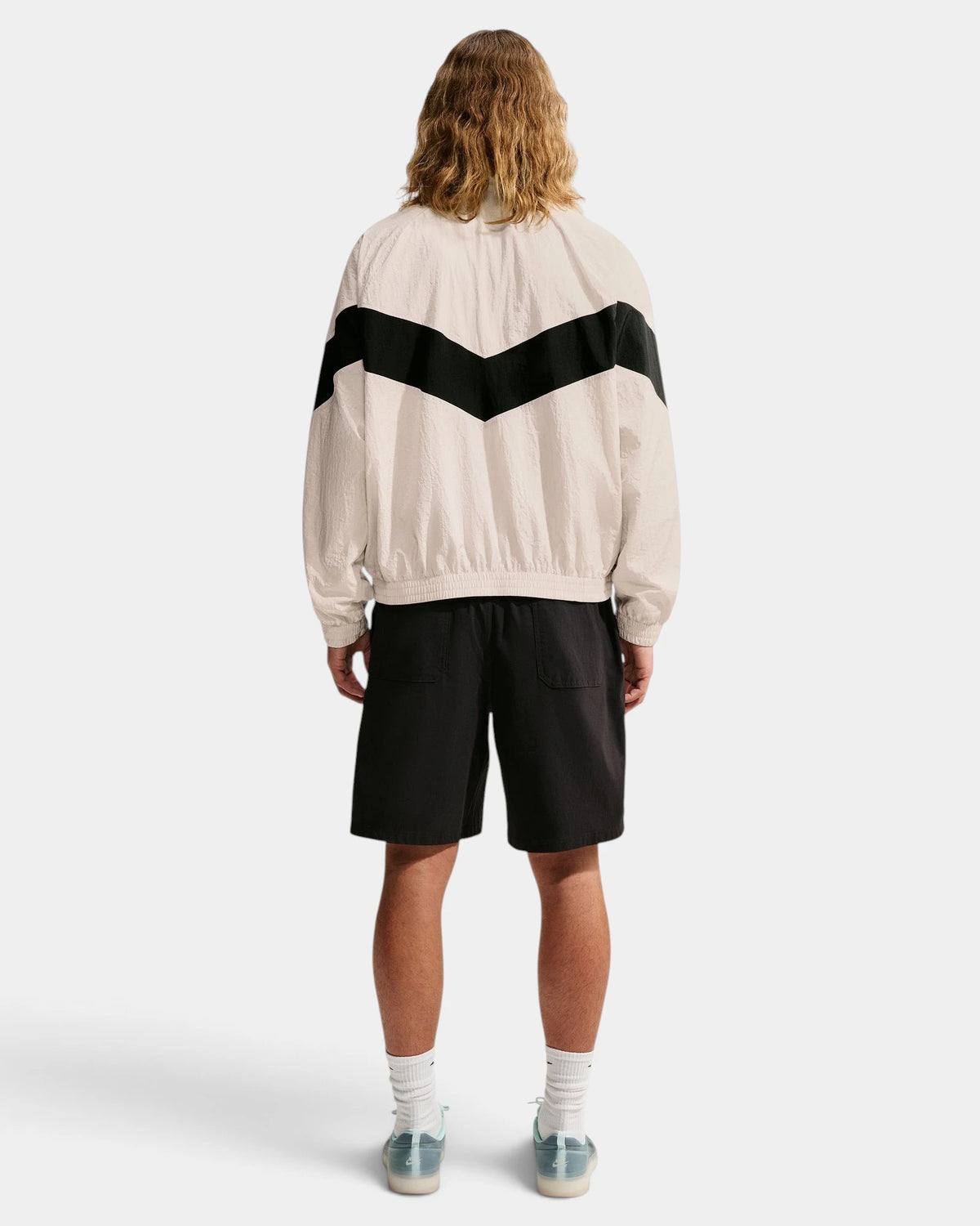 Back view of the Nike SB Pavan Jacket on a model, showing the black chevron across the shoulders and the elastic hem