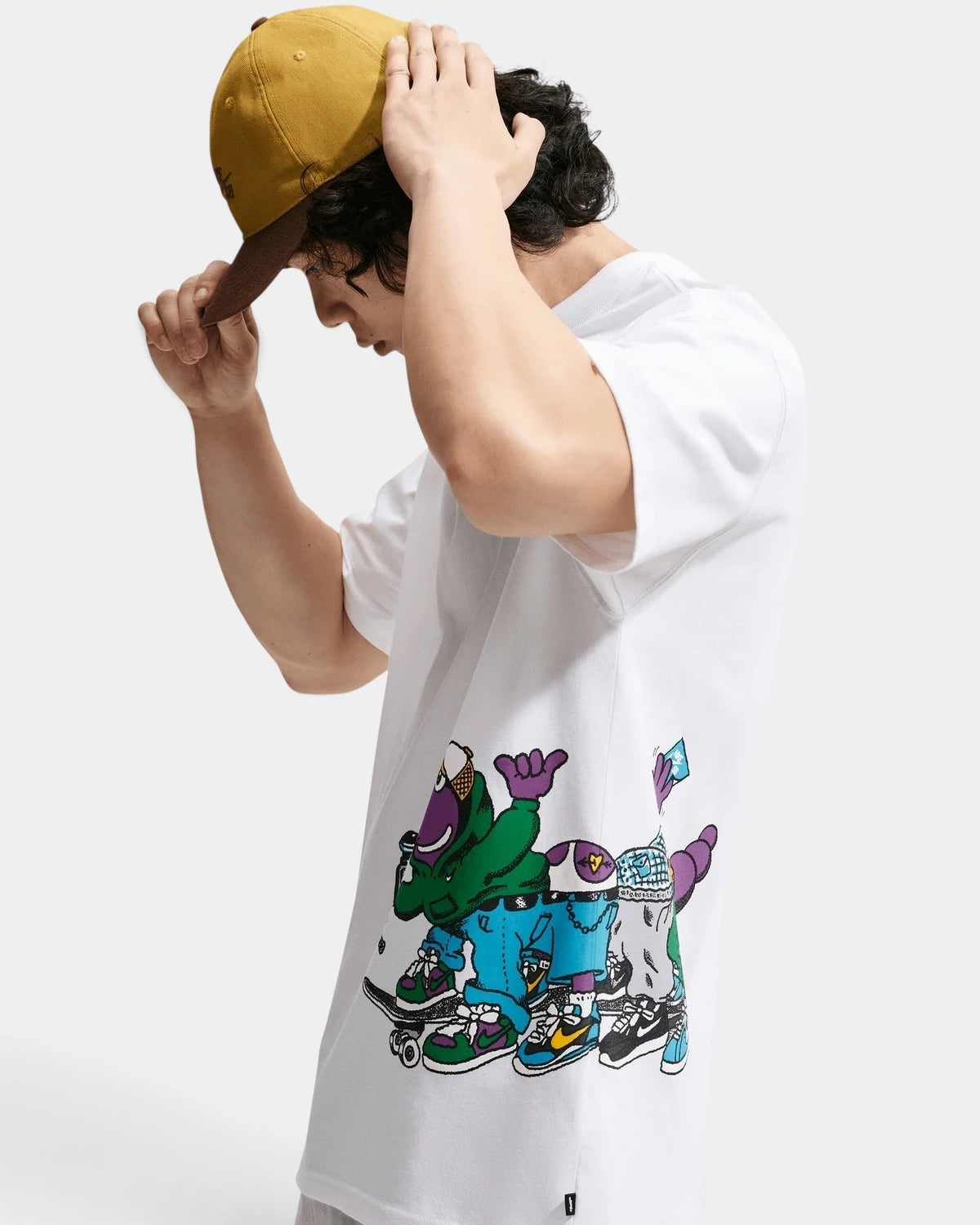 Model in the Nike SB Sk8pillar T-Shirt, side view of the graphic of cartoon caterpillars on skateboards wrapping round the hem