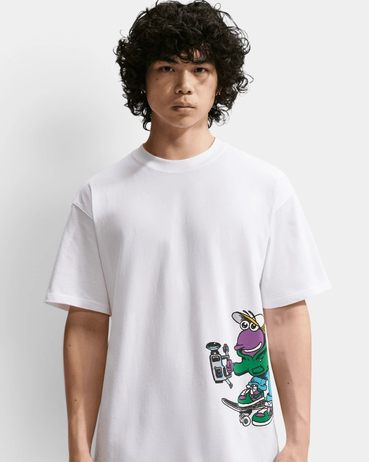 Model wearing the white Nike SB Sk8pillar T-Shirt, front view of the purple caterpillar filming with a camcorder on a skateboard