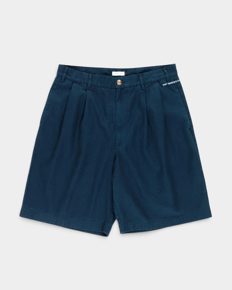 Pop Trading Company Boat Shorts in navy, flat lay front view showing the wide pleated leg, tortoise button and zip fly, and the white embroidered script logo above the left side pocket