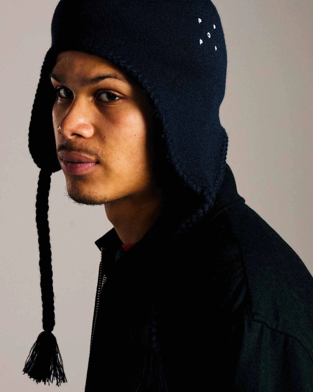 Lockwood Avenue model wearing the Pop Trading Company Reversible Earflap Beanie on the solid navy side, side view with a braided strap hanging down