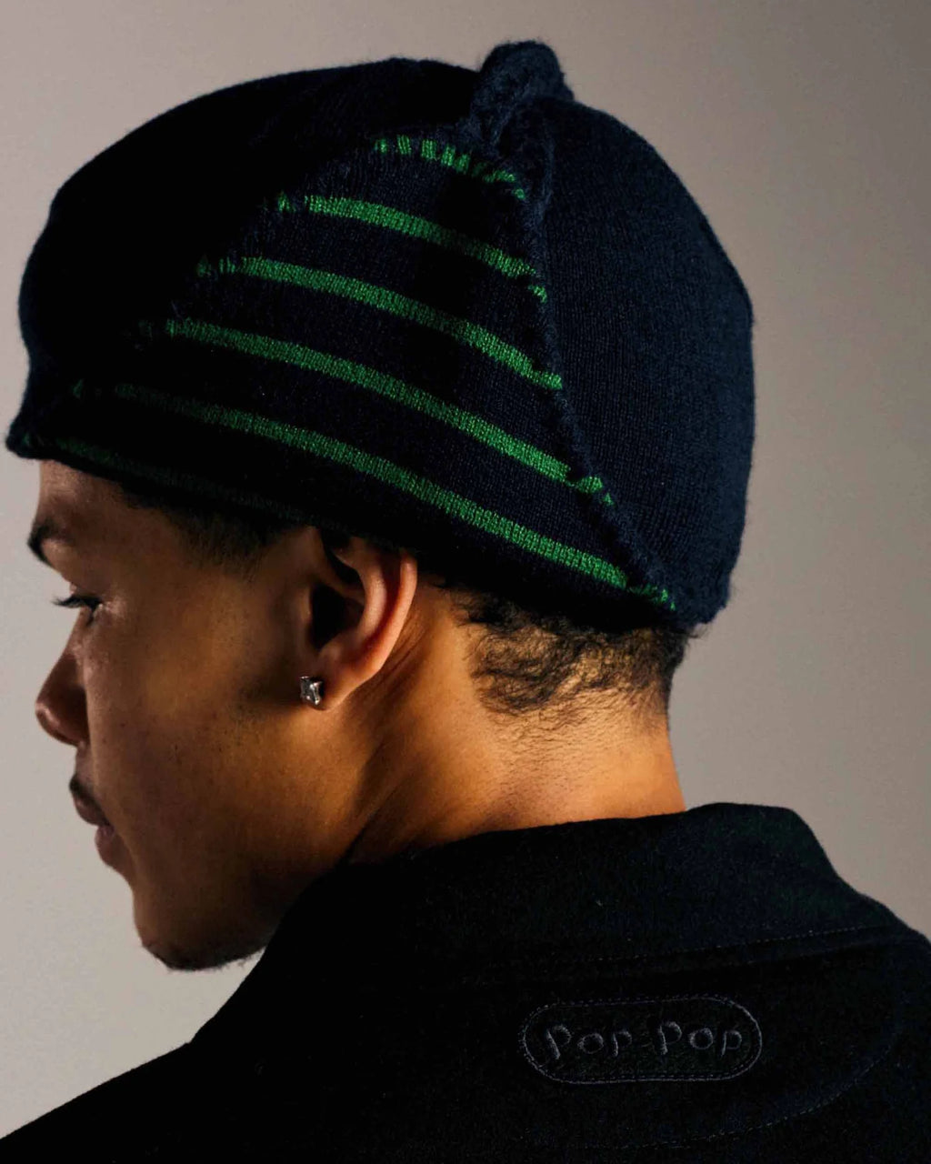 Lockwood Avenue model wearing the Pop Trading Company Reversible Earflap Beanie, back view showing the navy and juniper green striped earflap