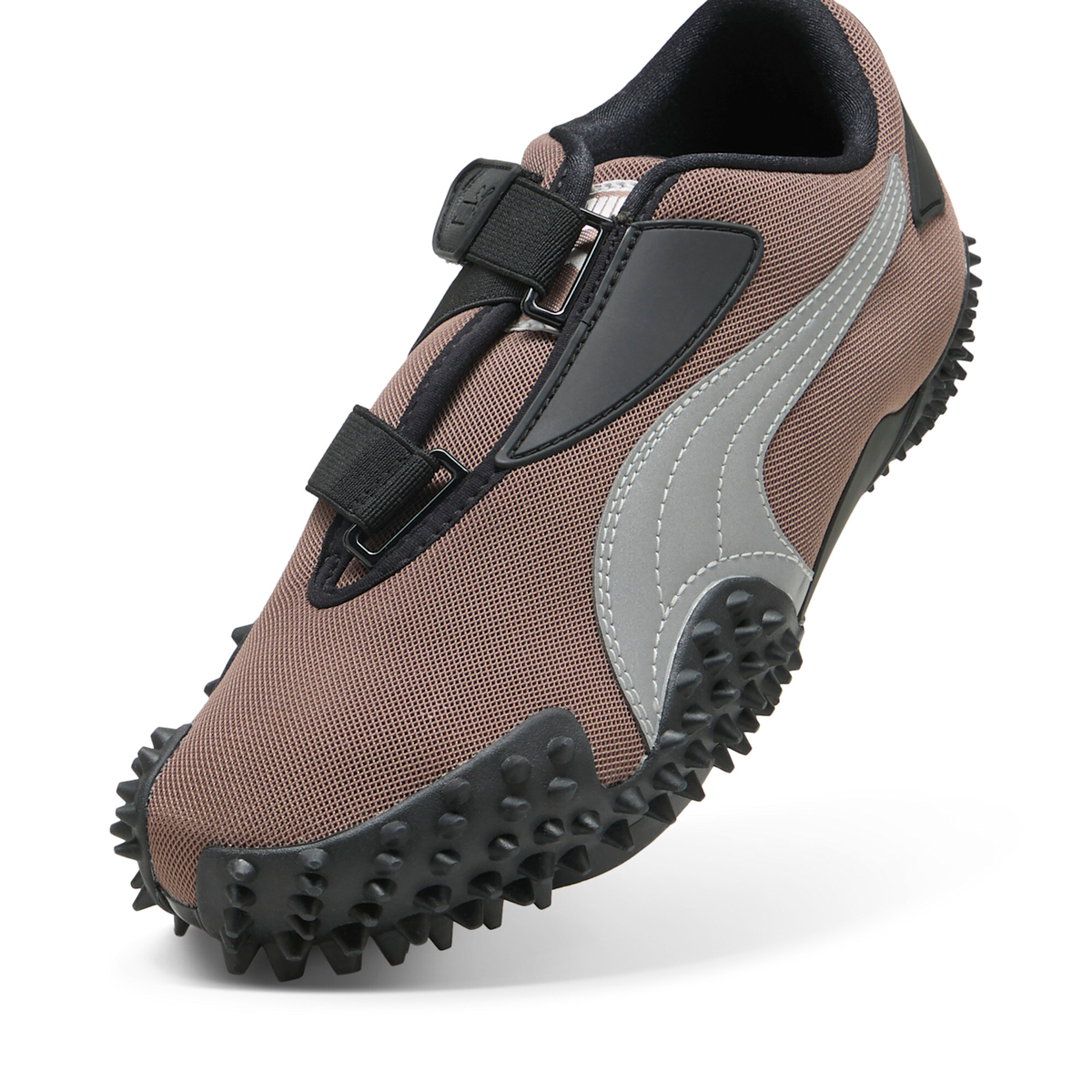 Close three-quarter front view of the Puma Mostro OG in Dark Clove, showing the strap hardware, the black toe cage and the silver formstrip against the brown mesh