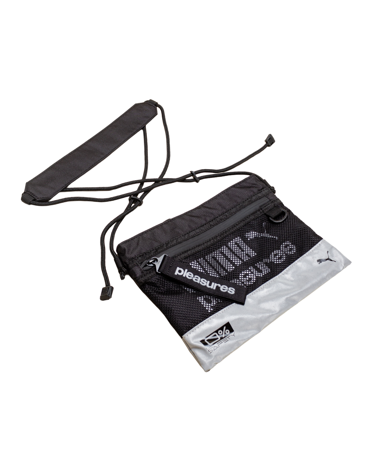 Puma x PLEASURES Body Bag in black, the whole flat crossbody laid out front on with its adjustable cord strap and removable padded shoulder pad beside it, showing the black mesh front panel, the reflective silver base and the Puma cat logo