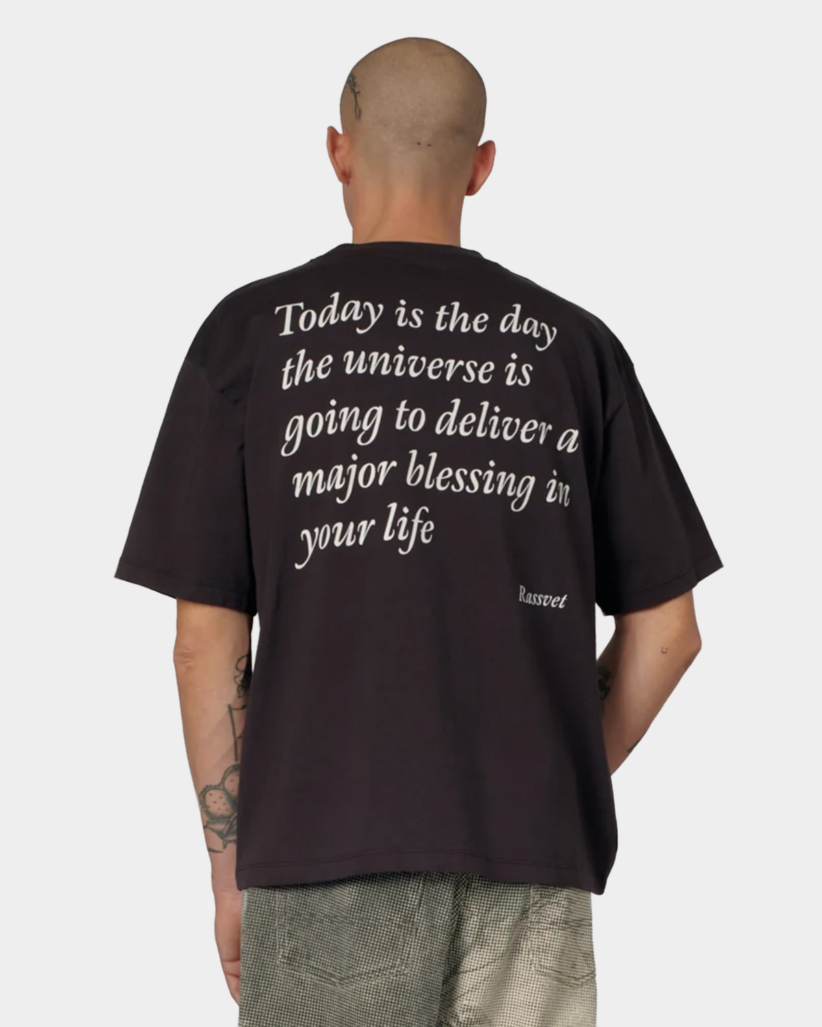 The same man from behind, showing the cream serif blessing text printed across the back of the brown tee