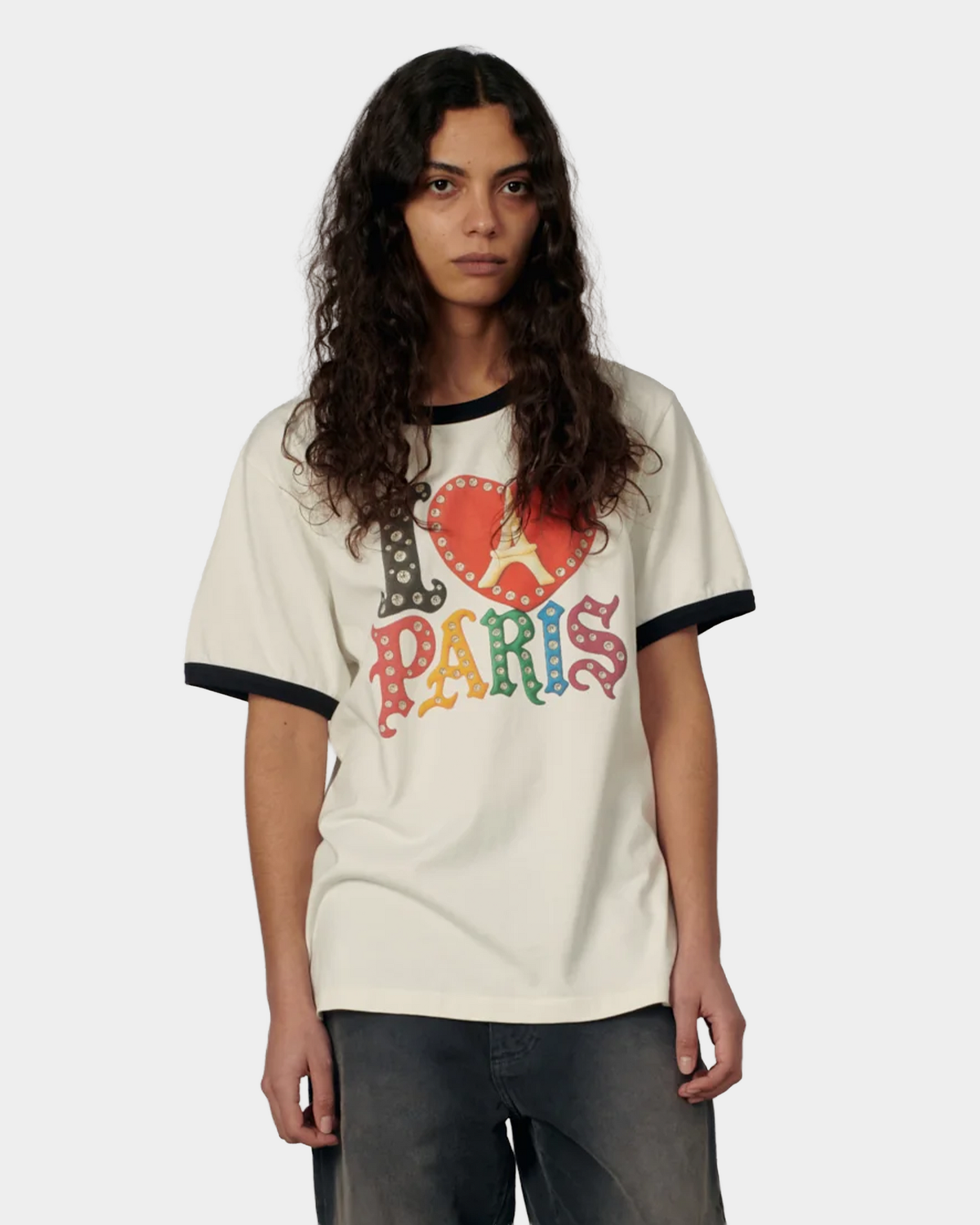 A model with long curly hair wearing the off white Rassvet Jewel Ringer T-Shirt, the multicolored I love Paris print across the chest